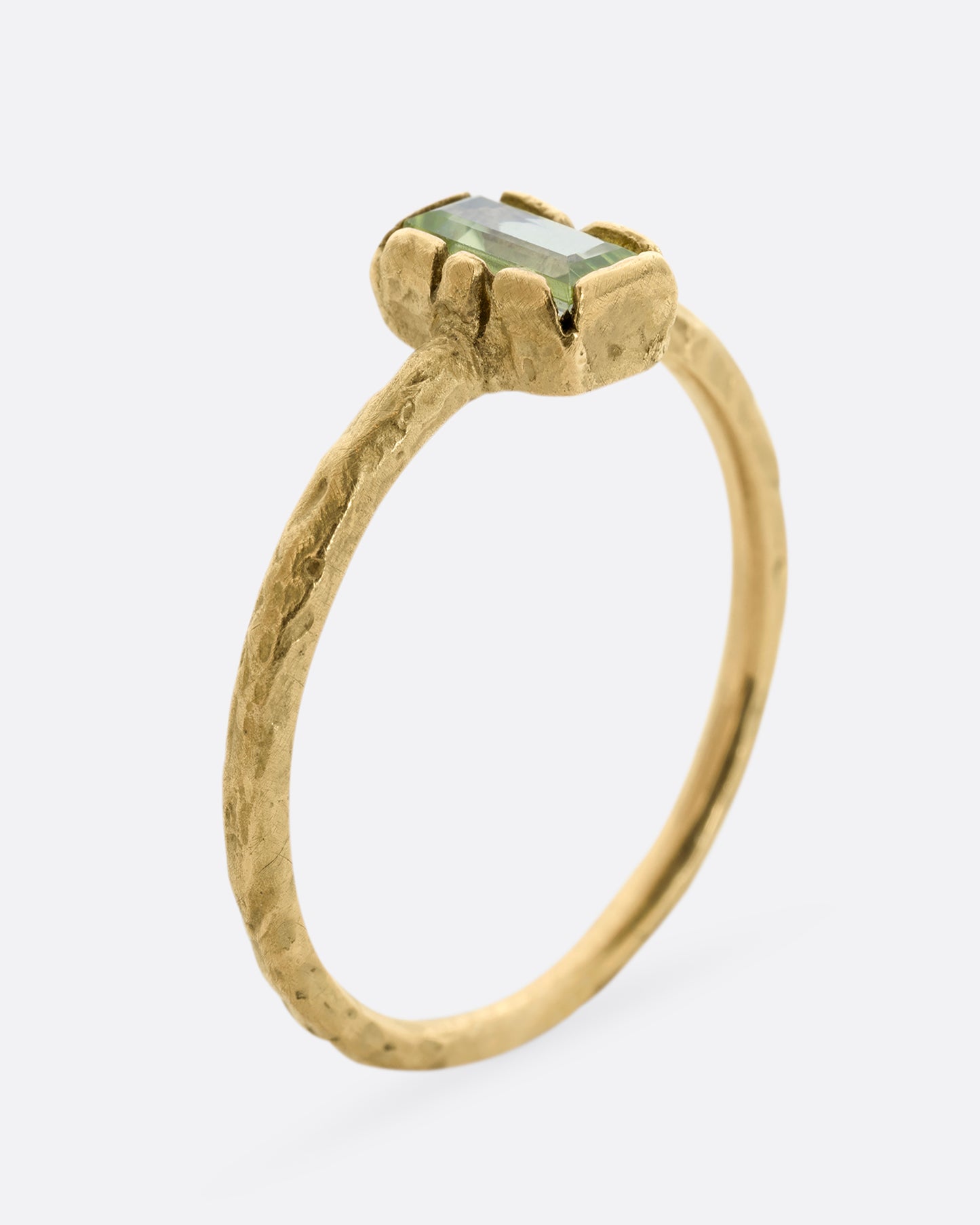 A textured yellow gold ring with a rectangular peridot. Shown from the side, standing up.