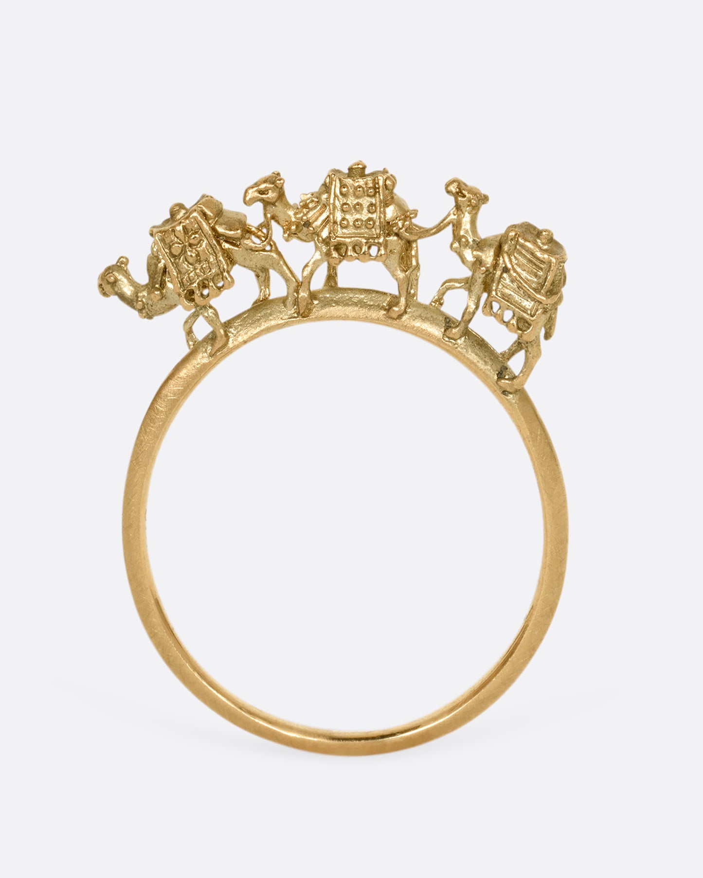 A yellow gold ring with a caravan of three camels walking across the top of the band. Shown from the front standing up.