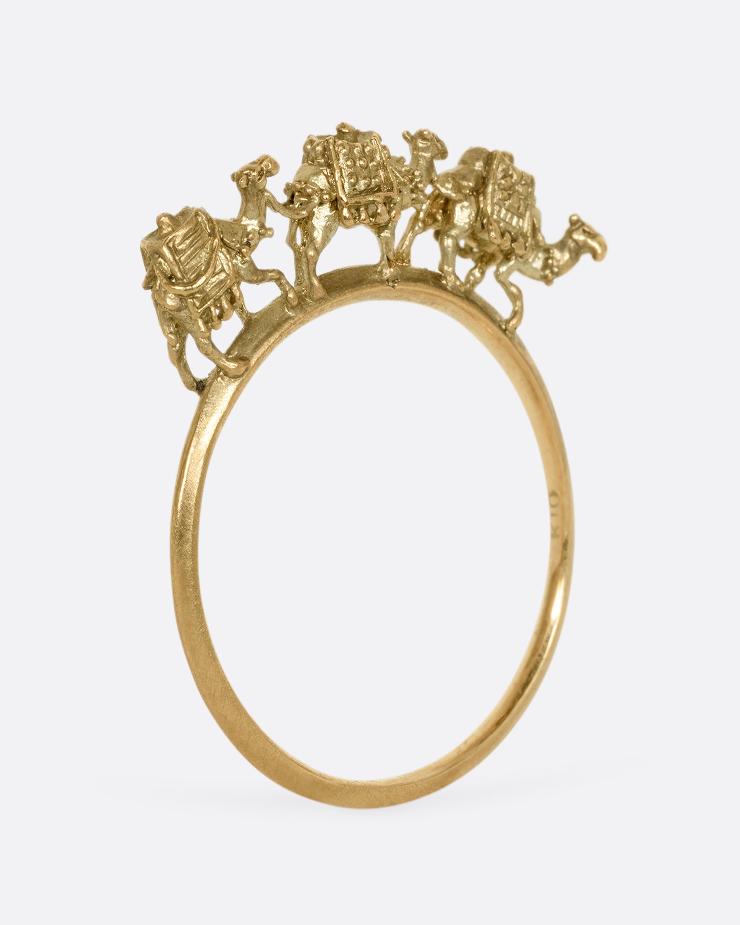 A yellow gold ring with a caravan of three camels walking across the top of the band. Shown from the side standing up.