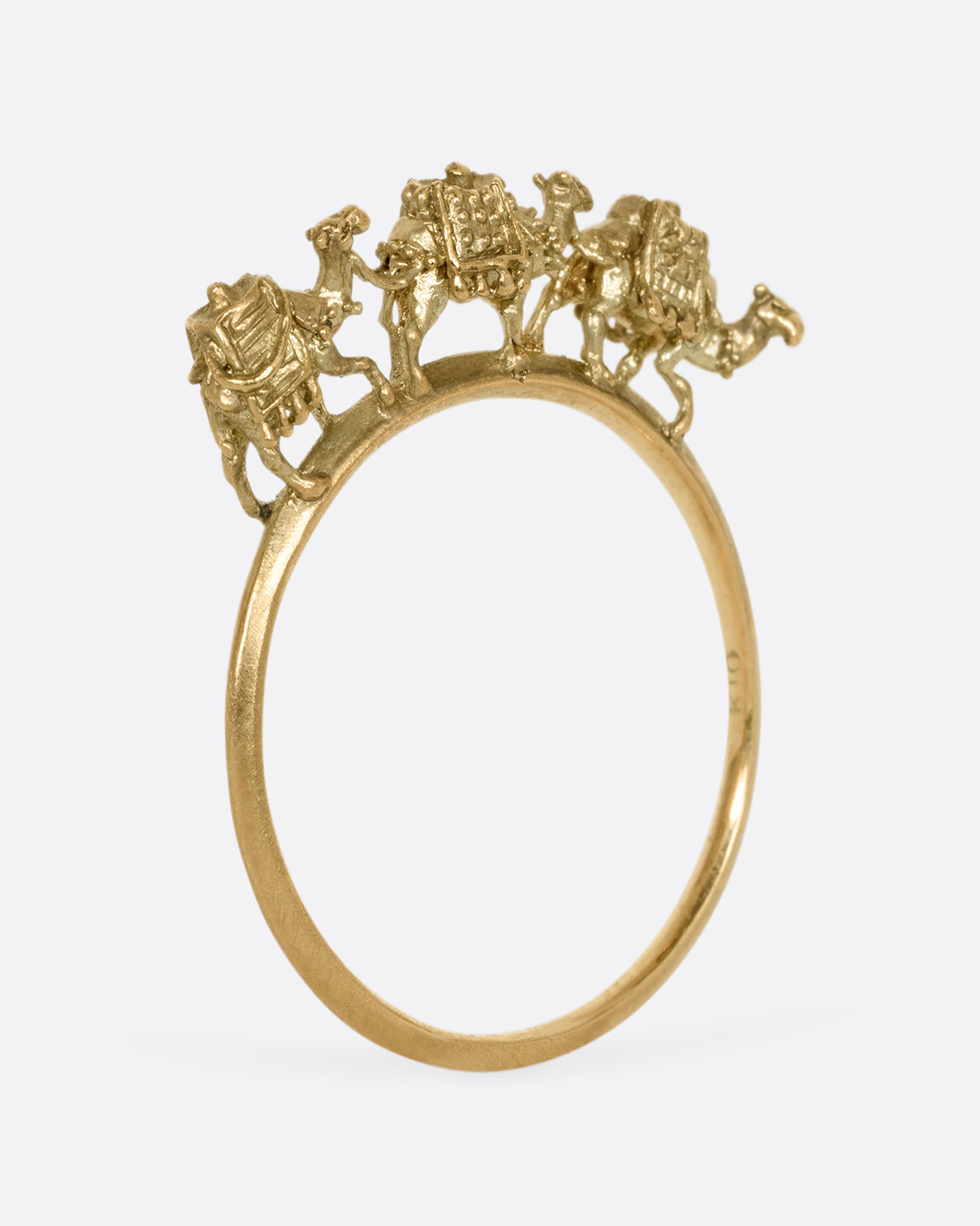 A yellow gold ring with a caravan of three camels walking across the top of the band. Shown from the side standing up.