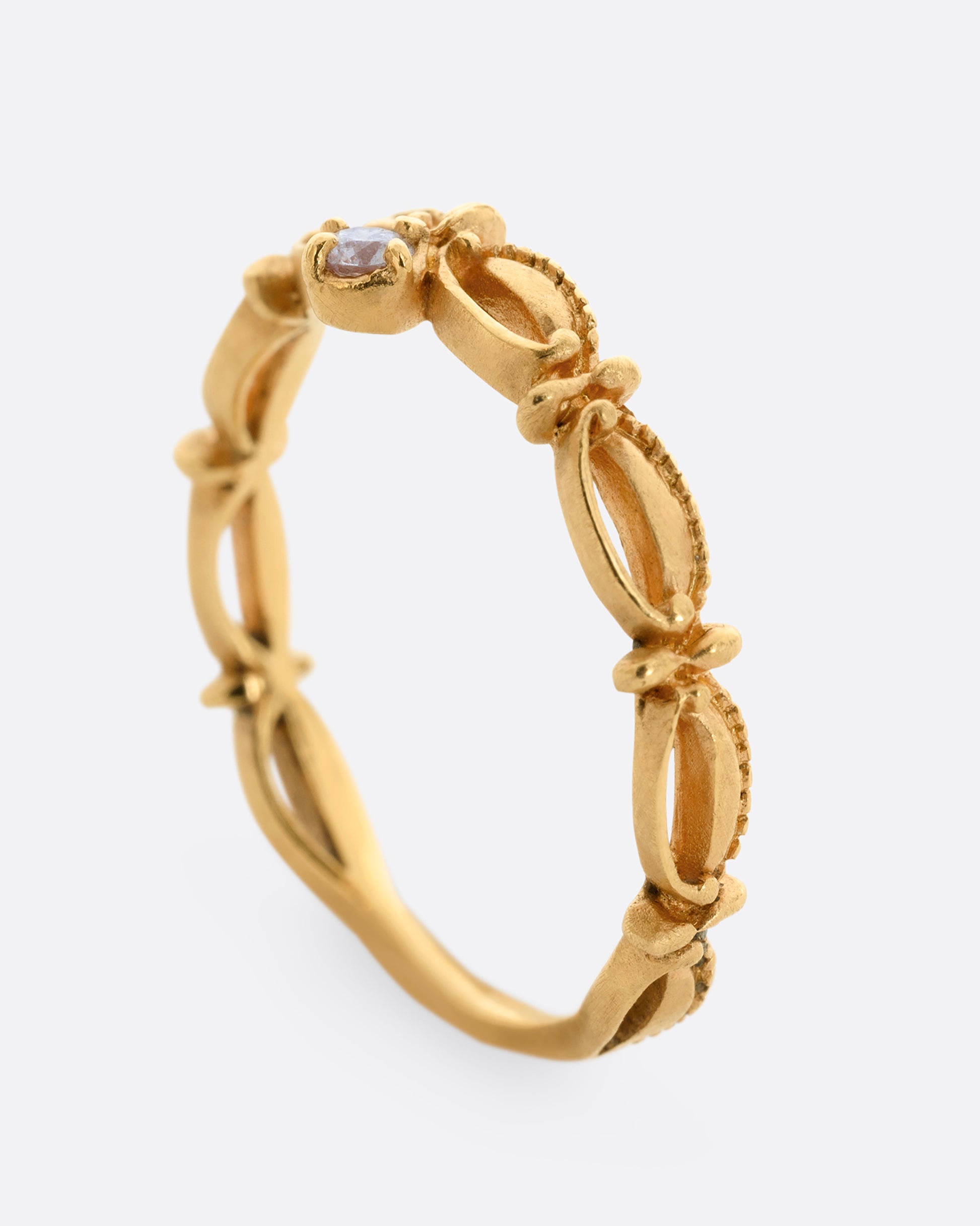 A yellow gold tiara shaped band with curved and textured details and a round white diamond at the center. Shown from the side, standing up.