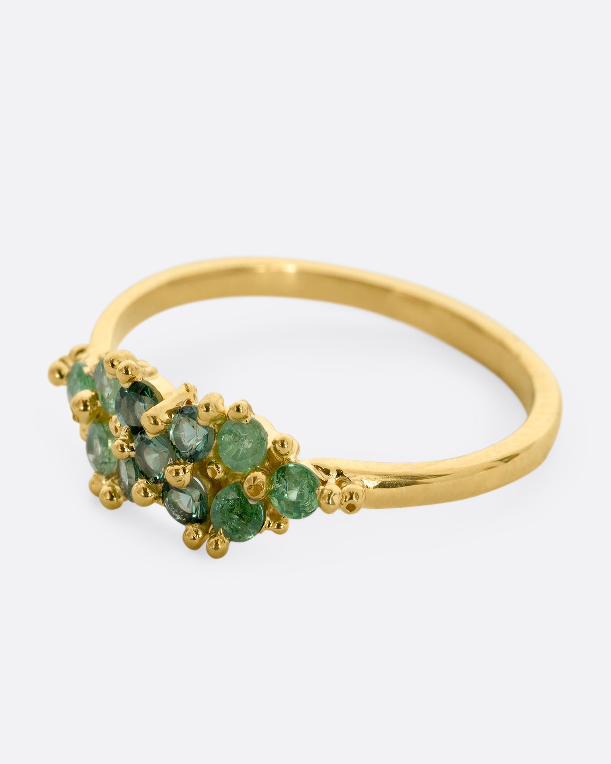 A yellow gold ring with a cluster of eleven green sapphires and tsavorite. Shown from the side.