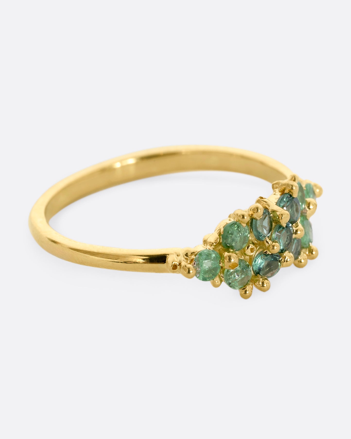 A yellow gold ring with a cluster of eleven green sapphires and tsavorite. Shown from the side.