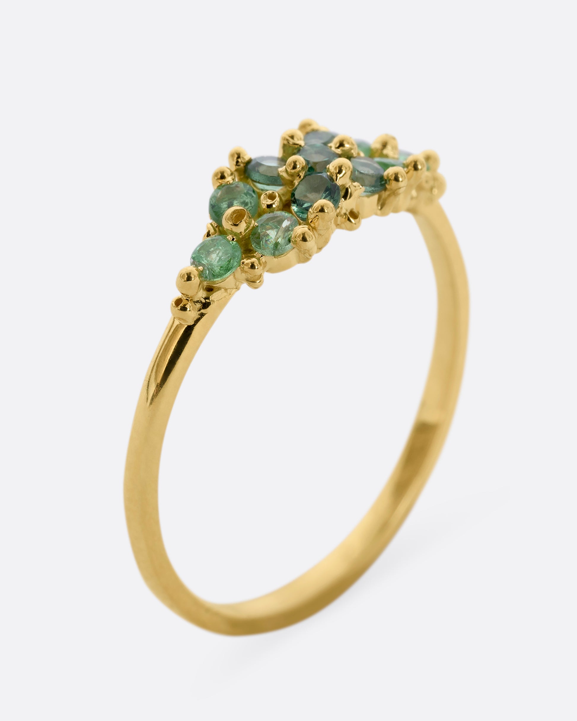A yellow gold ring with a cluster of eleven green sapphires and tsavorite. Shown from the side, standing up.