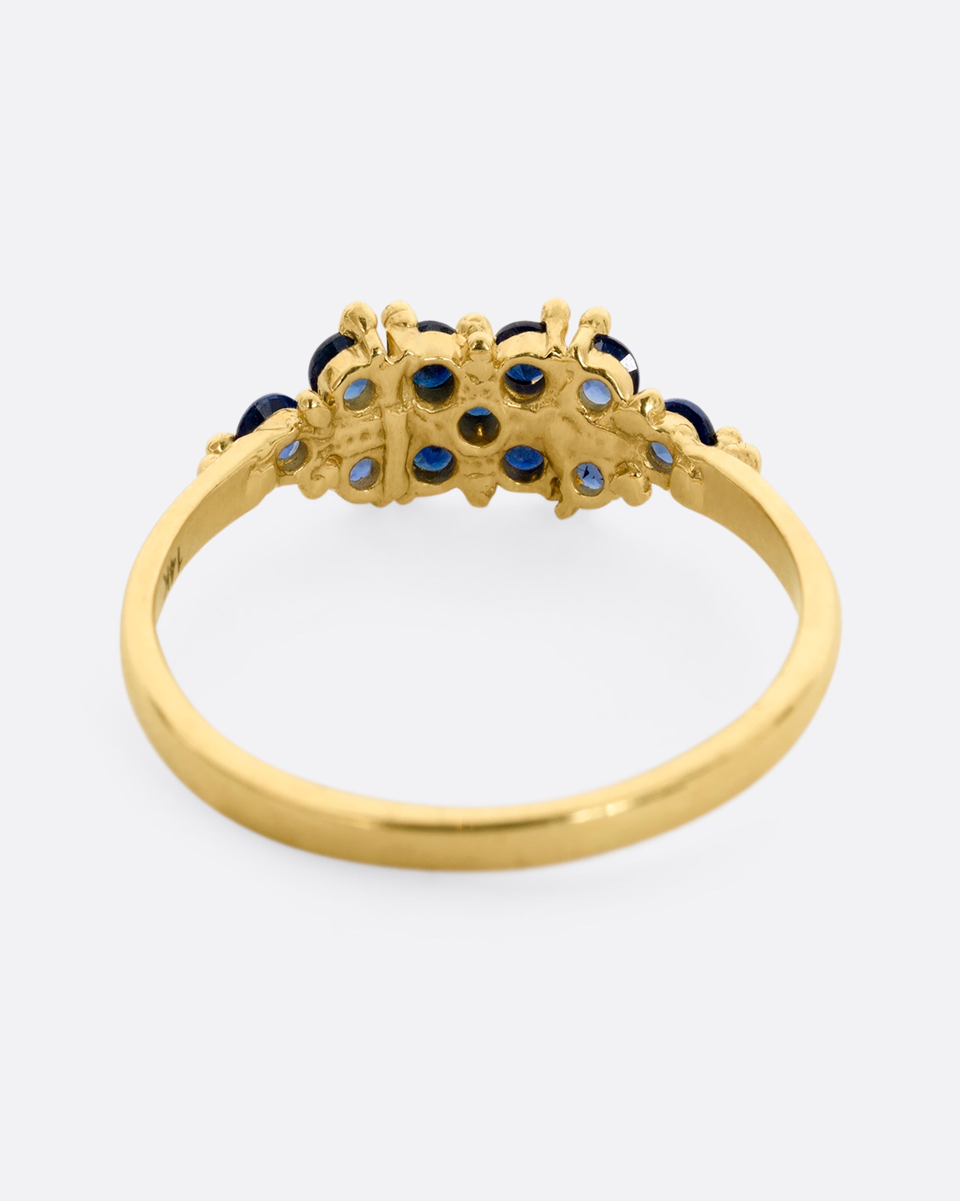A yellow gold ring with a cluster of eleven blue sapphires. Shown from the back.