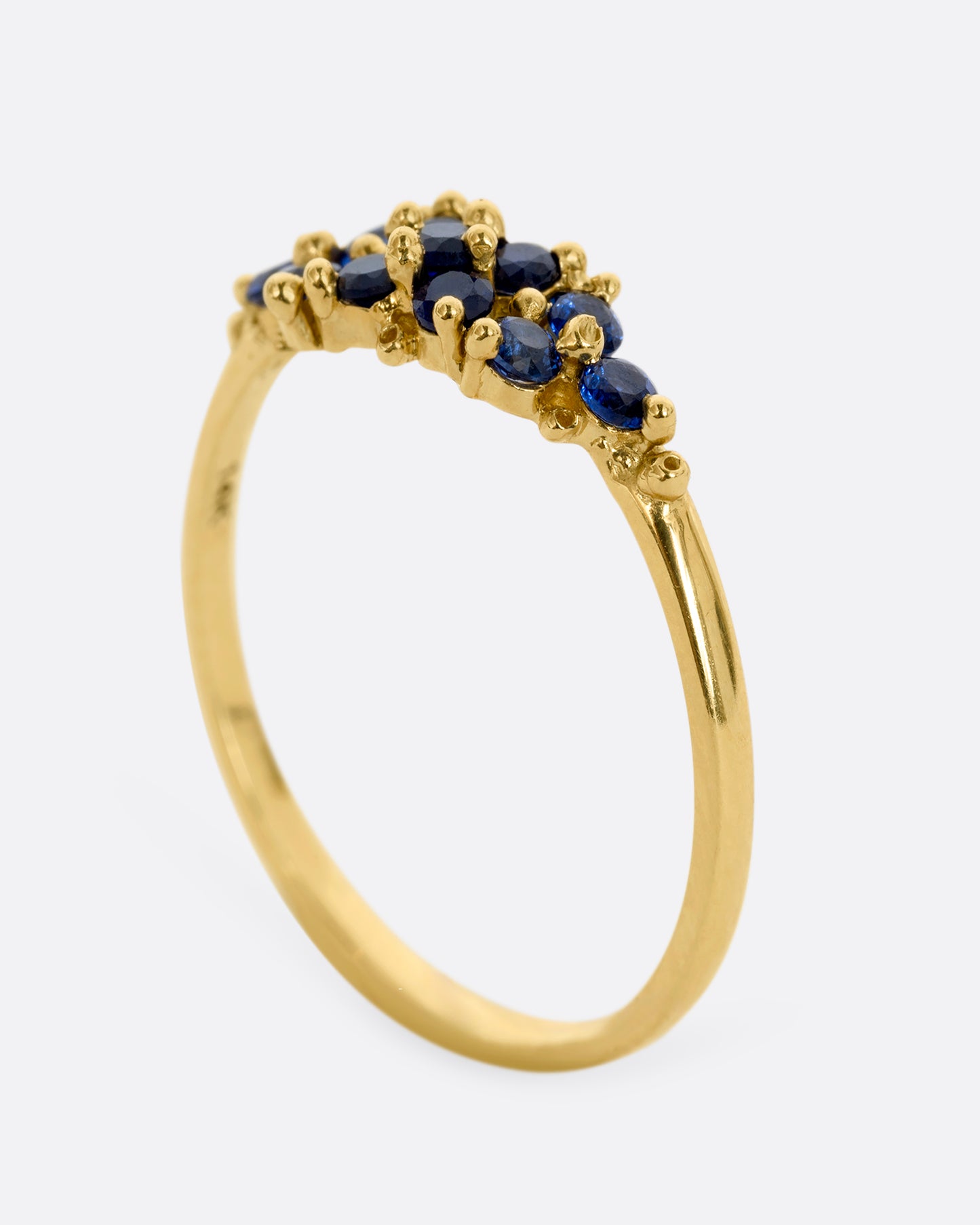A yellow gold ring with a cluster of eleven blue sapphires. Shown from the side, standing up.