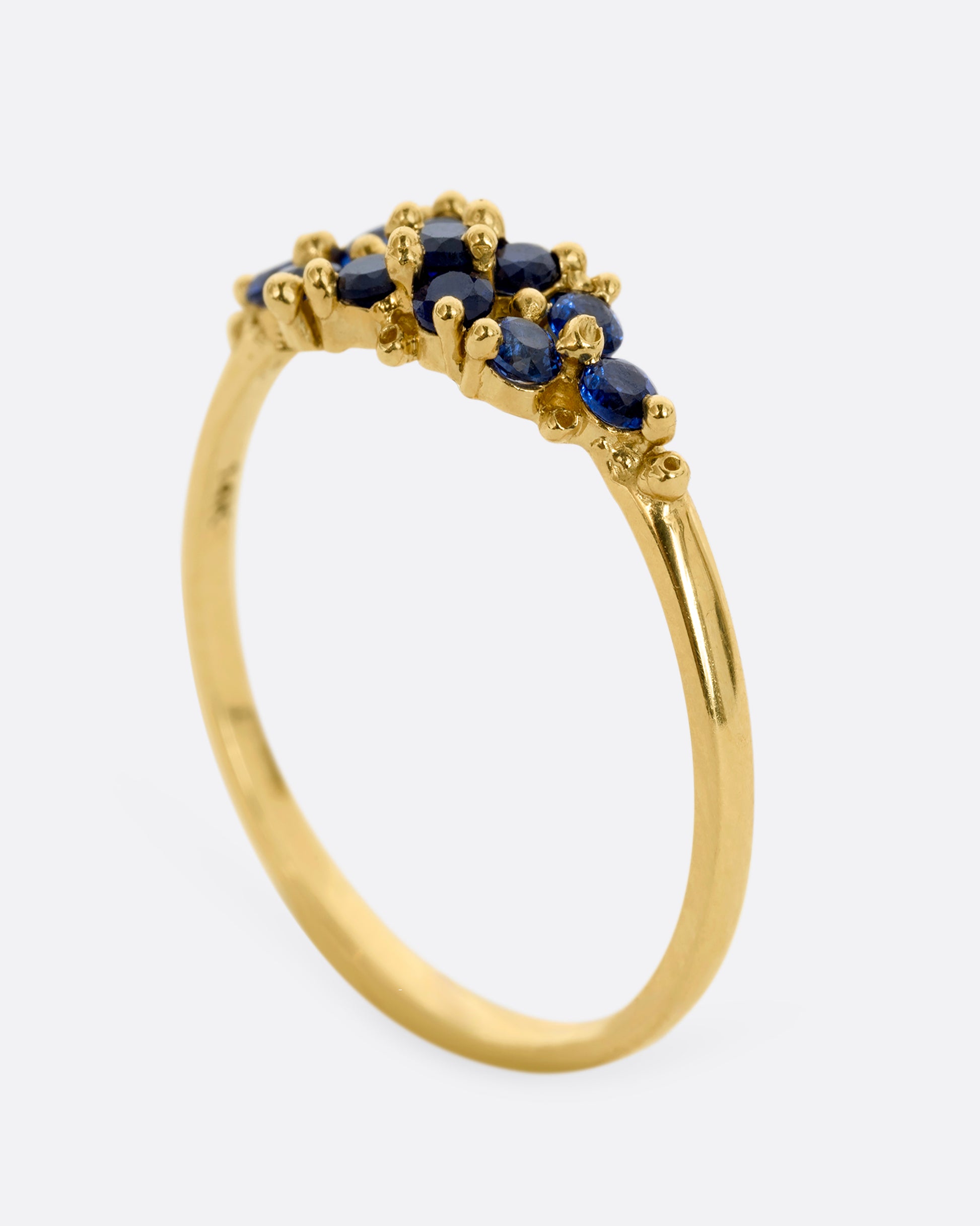 A yellow gold ring with a cluster of eleven blue sapphires. Shown from the side, standing up.
