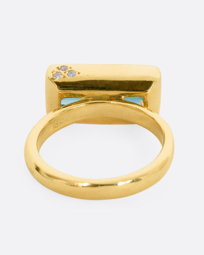 A yellow gold ring with a baguette indicolite tourmaline and small white diamonds. Shown from the back.