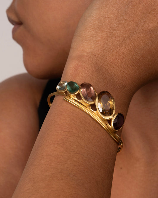 A yellow gold hinged bracelet crowned with five large different color tourmalines. Shown on a wrist from the front.