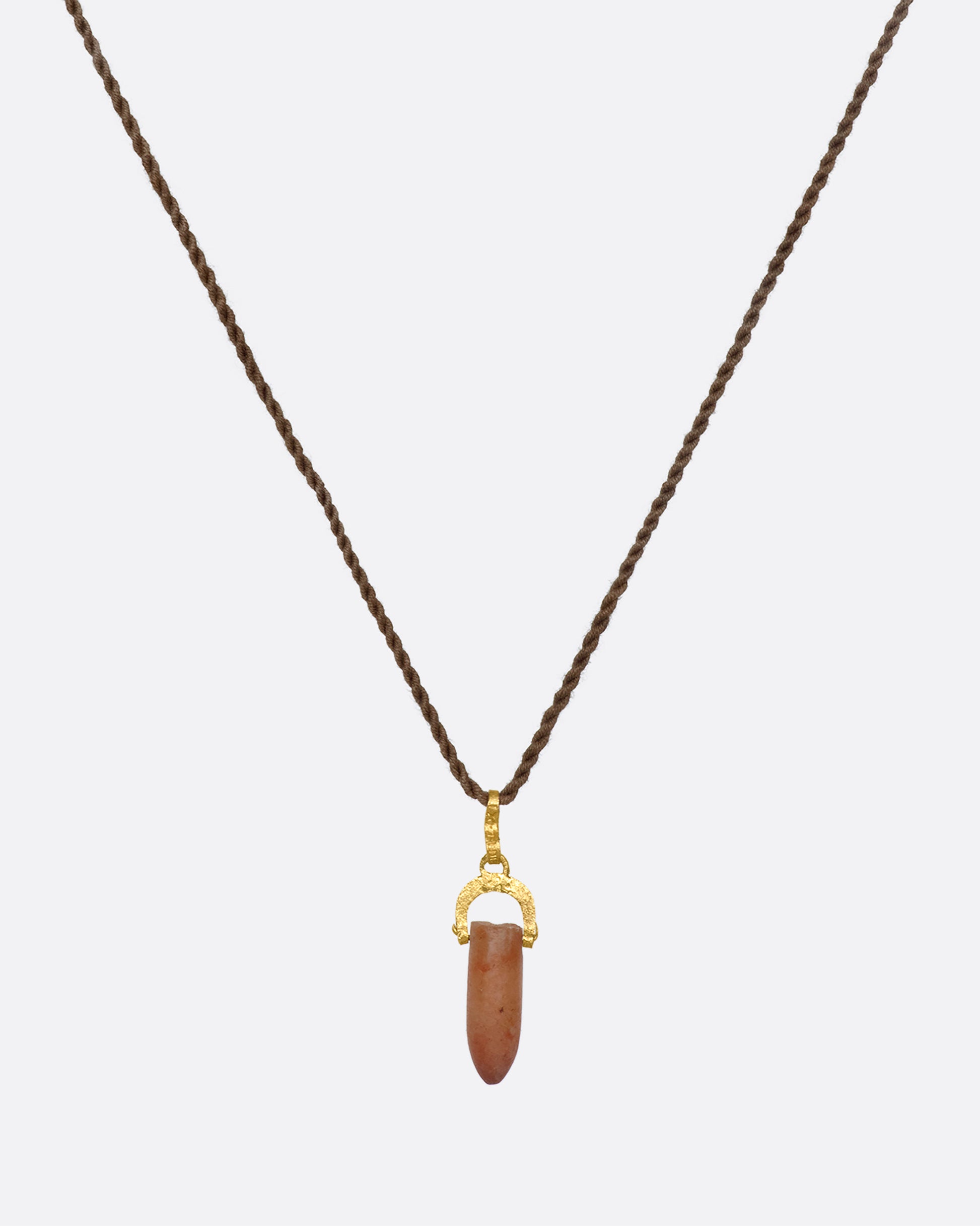 A stunning pre-Columbian carnelian bullet pendant suspended in 22k gold from a lengthy, twisted brown chord