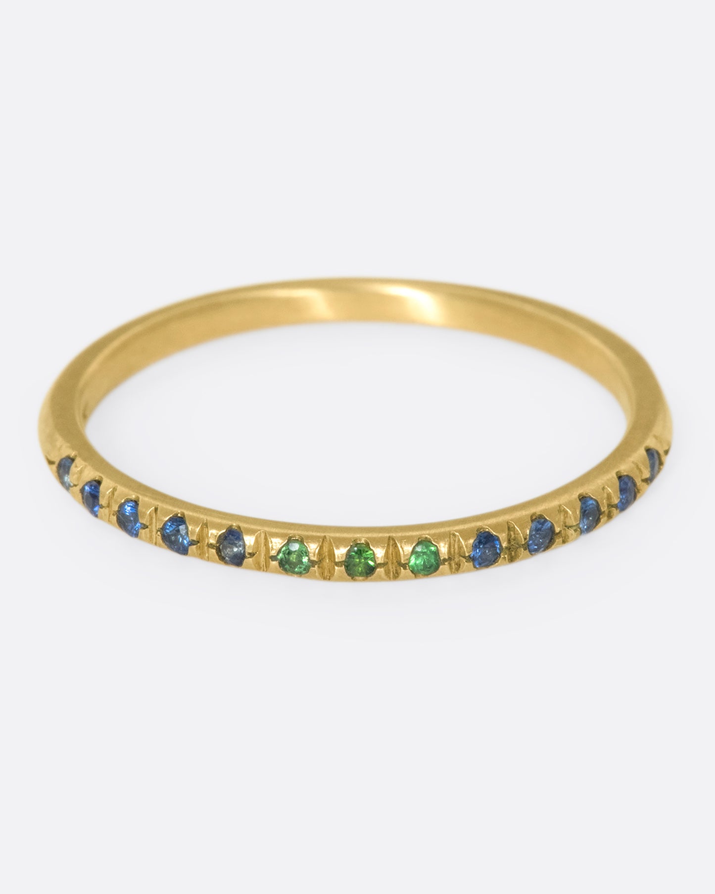 A thin yellow gold band with three green garnets set in the middle and five blue sapphires on either side. Shown from the front.
