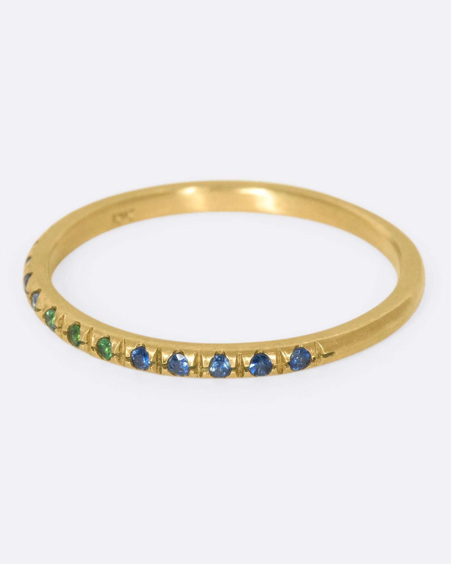 A thin yellow gold band with three green garnets set in the middle and five blue sapphires on either side. Shown from the side.