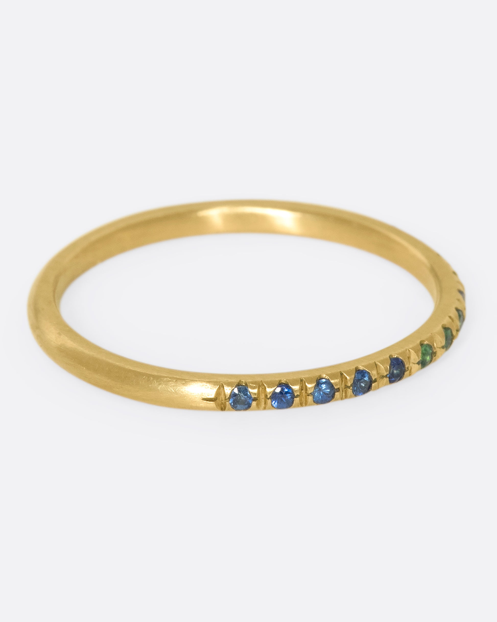 A thin yellow gold band with three green garnets set in the middle and five blue sapphires on either side. Shown from the side.