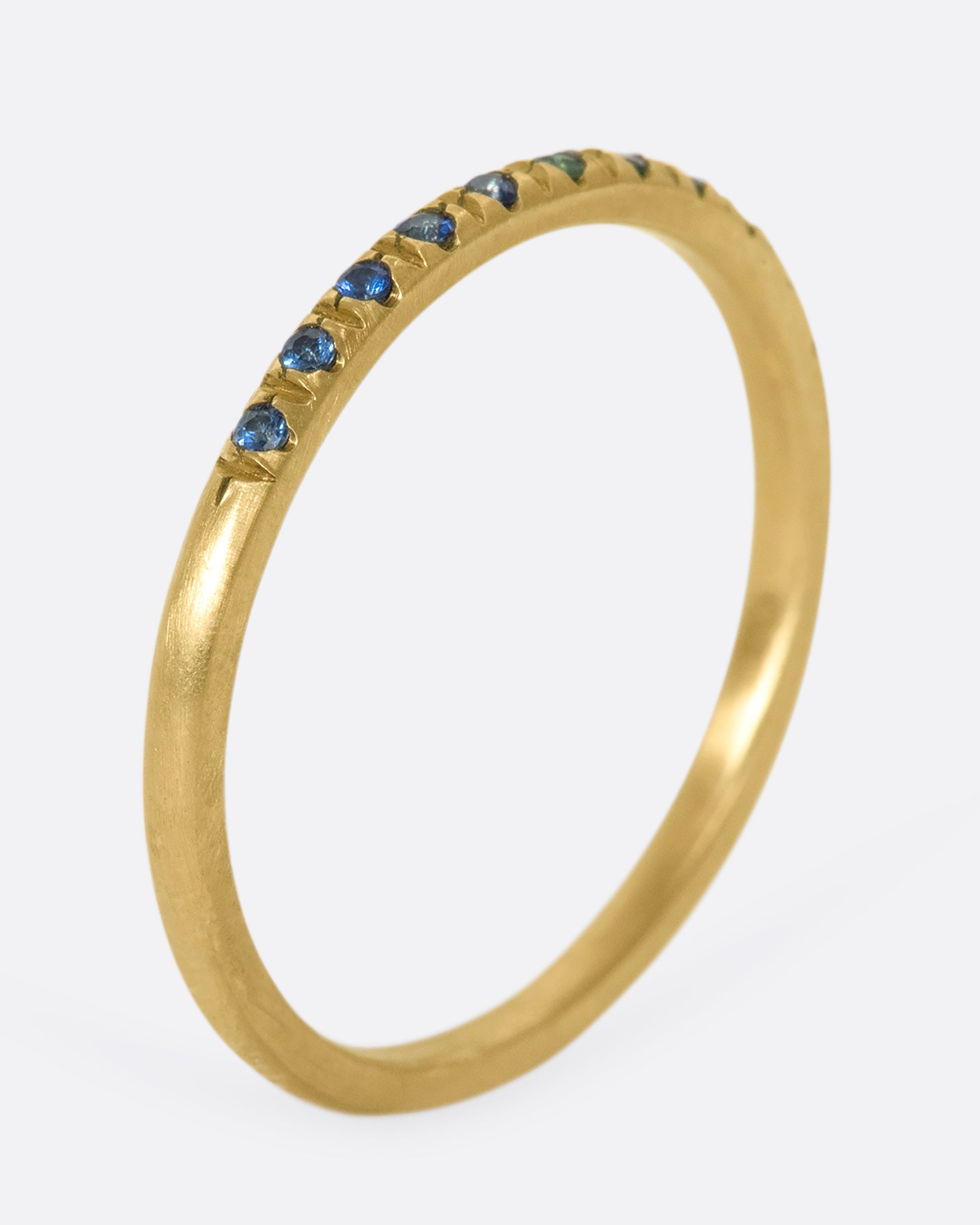 A thin yellow gold band with three green garnets set in the middle and five blue sapphires on either side. Shown standing up from the side.