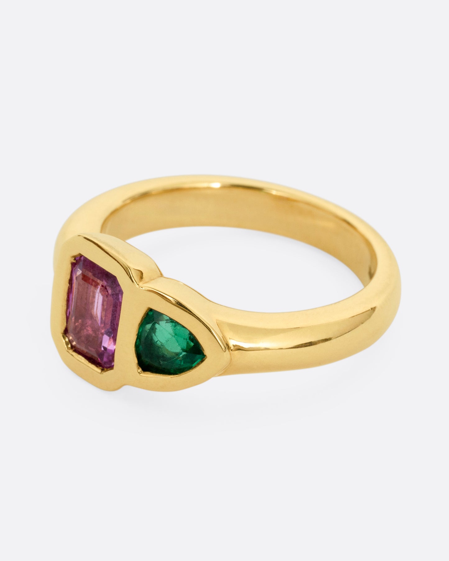 A yellow gold ring with an emerald and a pink sapphire, shown from the side.