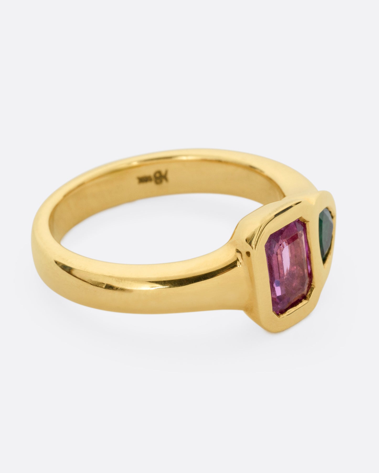 A yellow gold ring with an emerald and a pink sapphire, shown from the side.