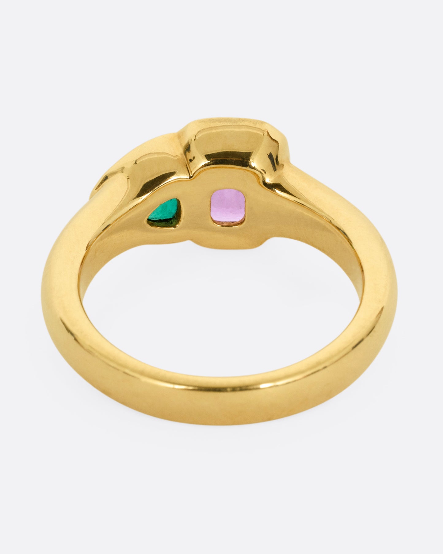 A yellow gold ring with an emerald and a pink sapphire, shown from the back.