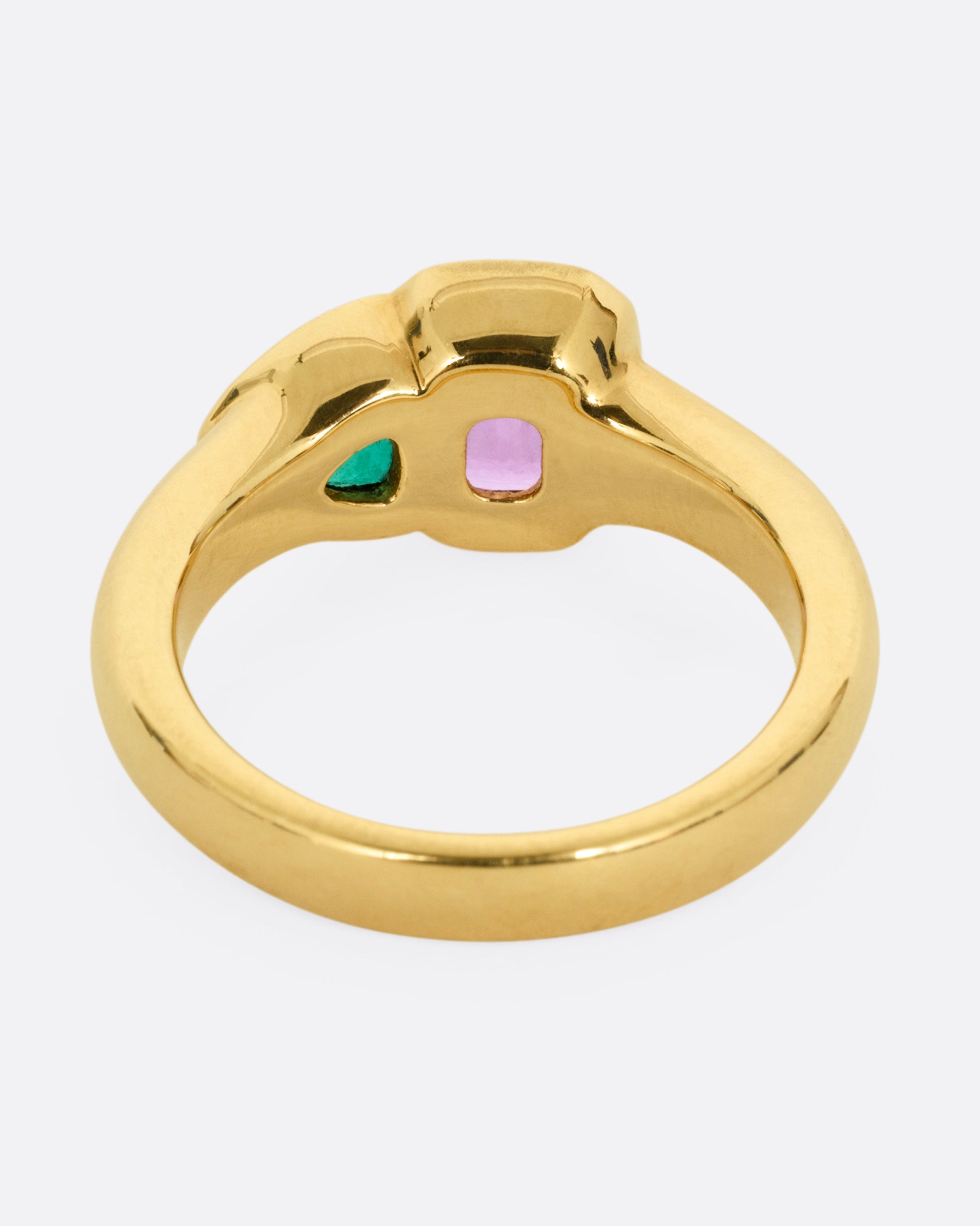 A yellow gold ring with an emerald and a pink sapphire, shown from the back.