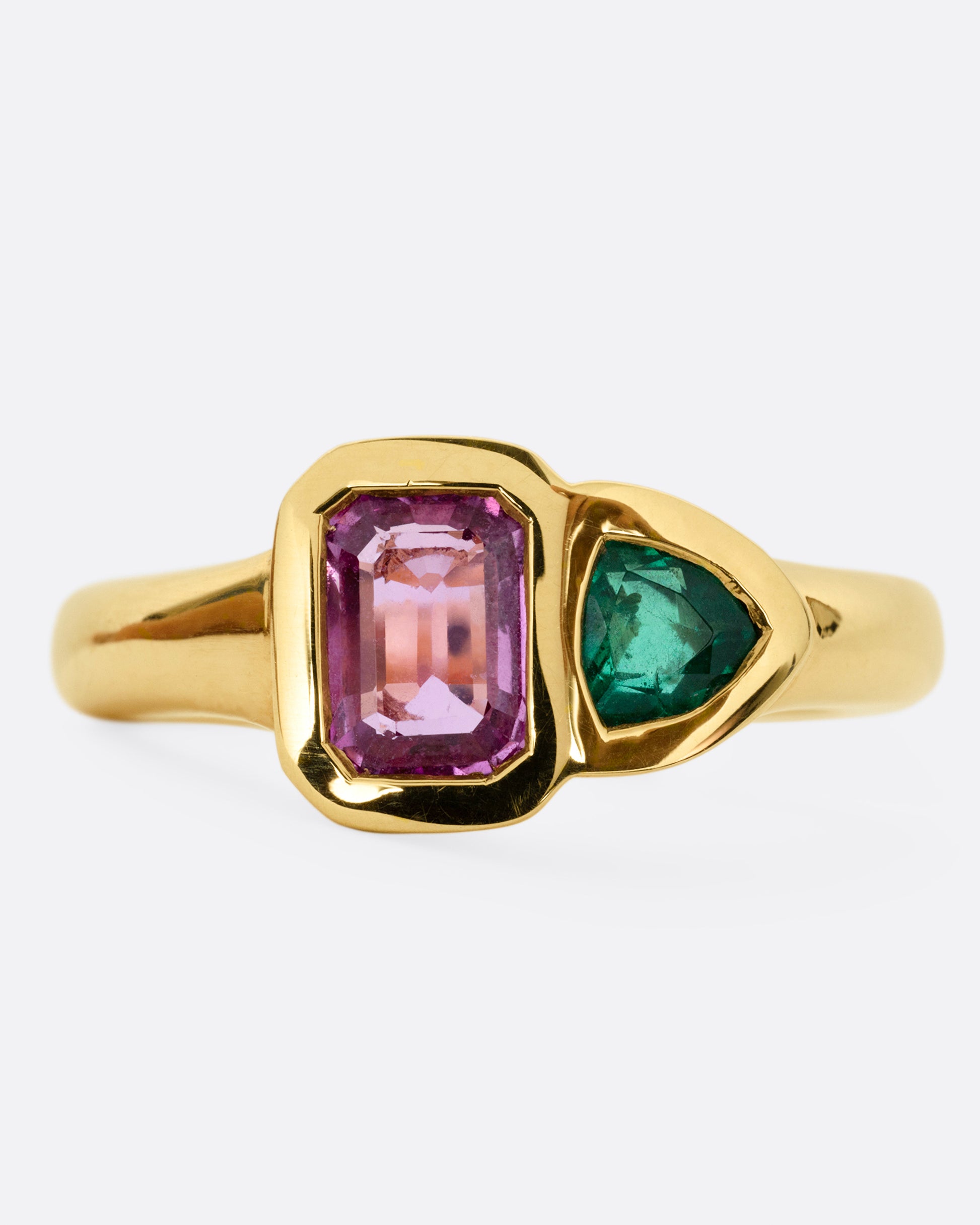 A yellow gold ring with an emerald and a pink sapphire, shown from the front.