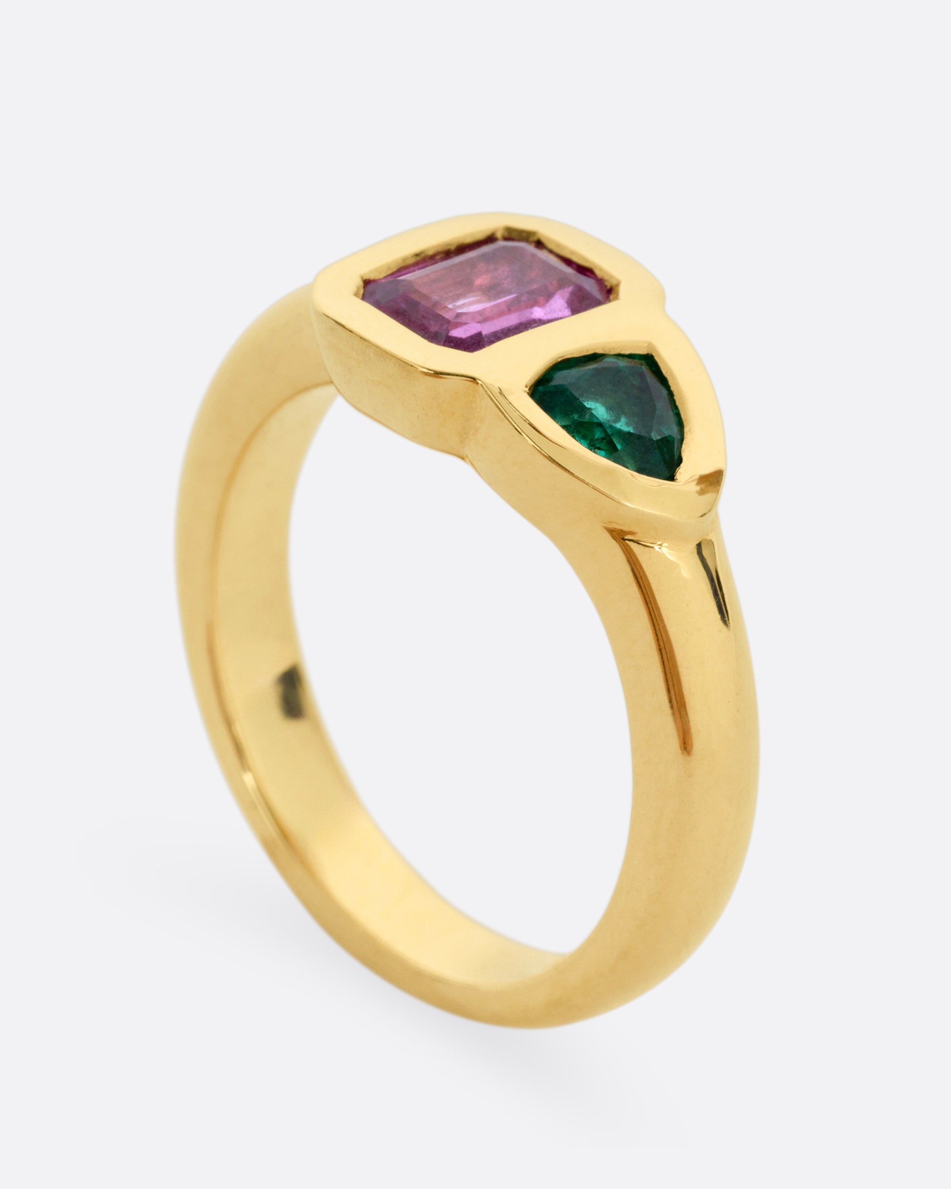 A yellow gold ring with an emerald and a pink sapphire, shown standing up from the side.