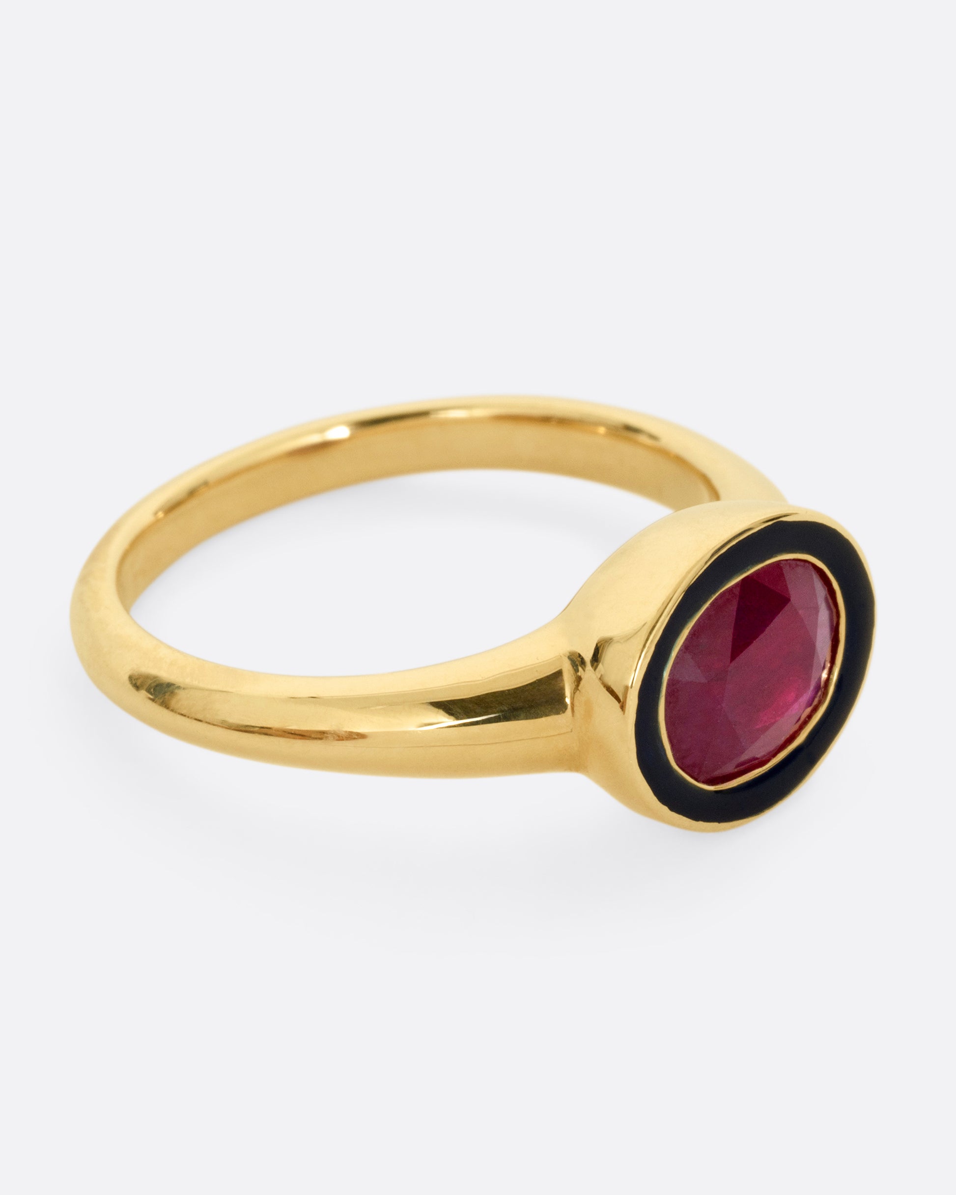 A yellow gold ring with a navy enamel and ruby center. Shown from the side.