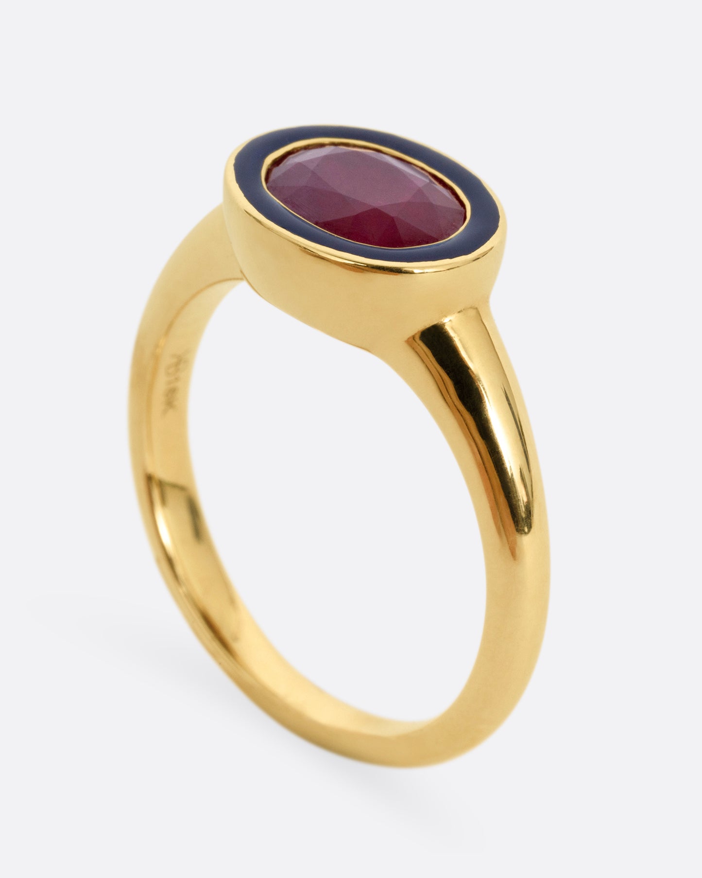 A yellow gold ring with a navy enamel and ruby center. Shown standing up from the side.