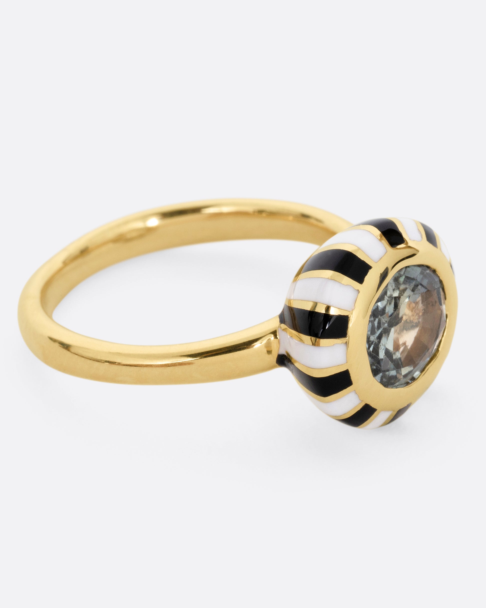 A yellow gold ring with an enamel checkerboard pattern around a green sapphire, shown from the side.