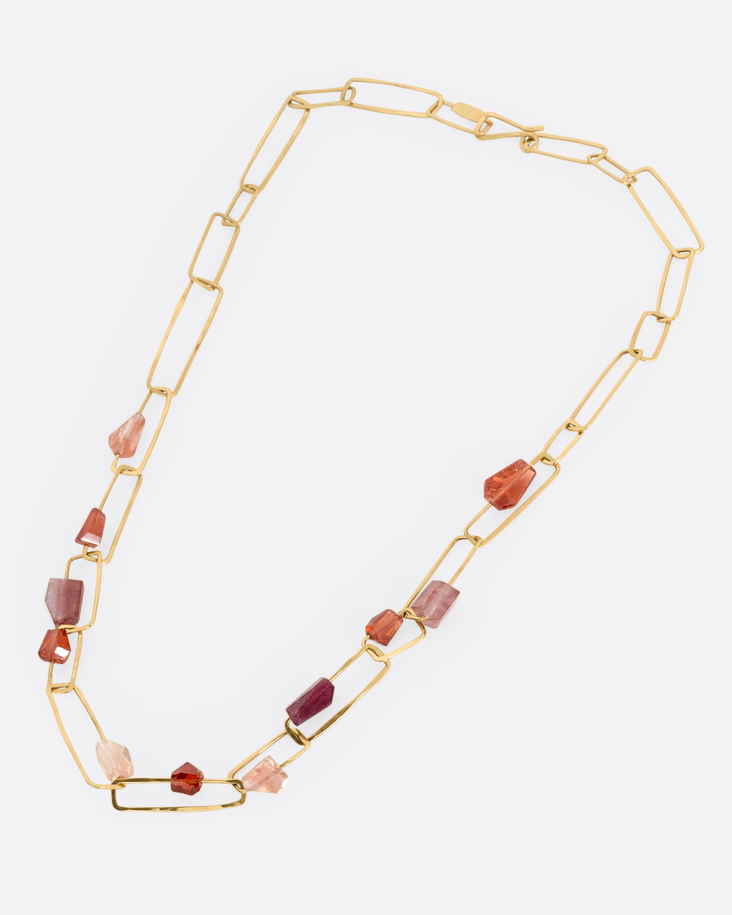 A yellow gold necklace with hammered paperclip links of differing sizes and freeform tourmalines, hessonite garnets, and Oregon sunstones, shown from the front.