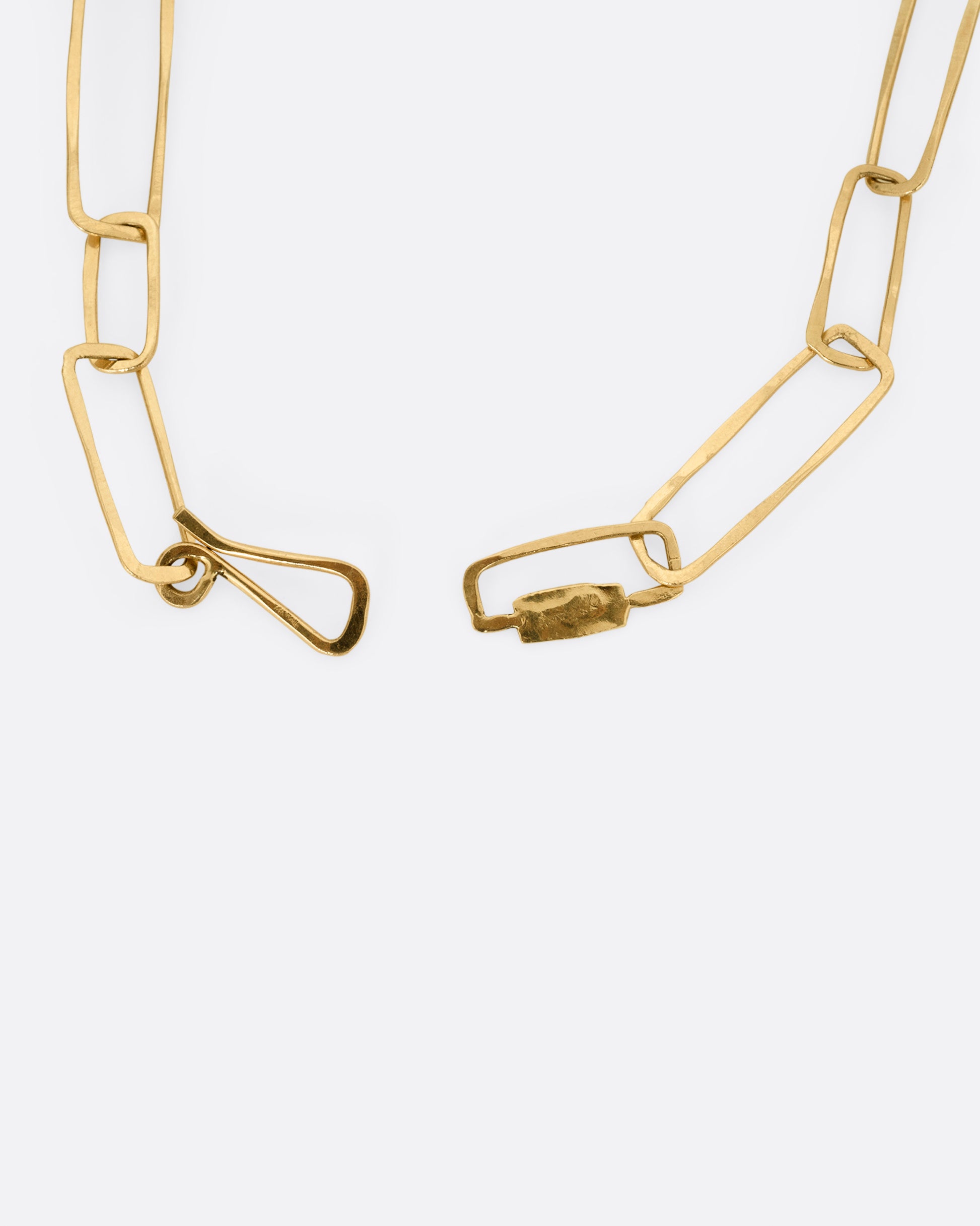 A close up of the clasp on a yellow gold necklace with hammered paperclip links of differing sizes.