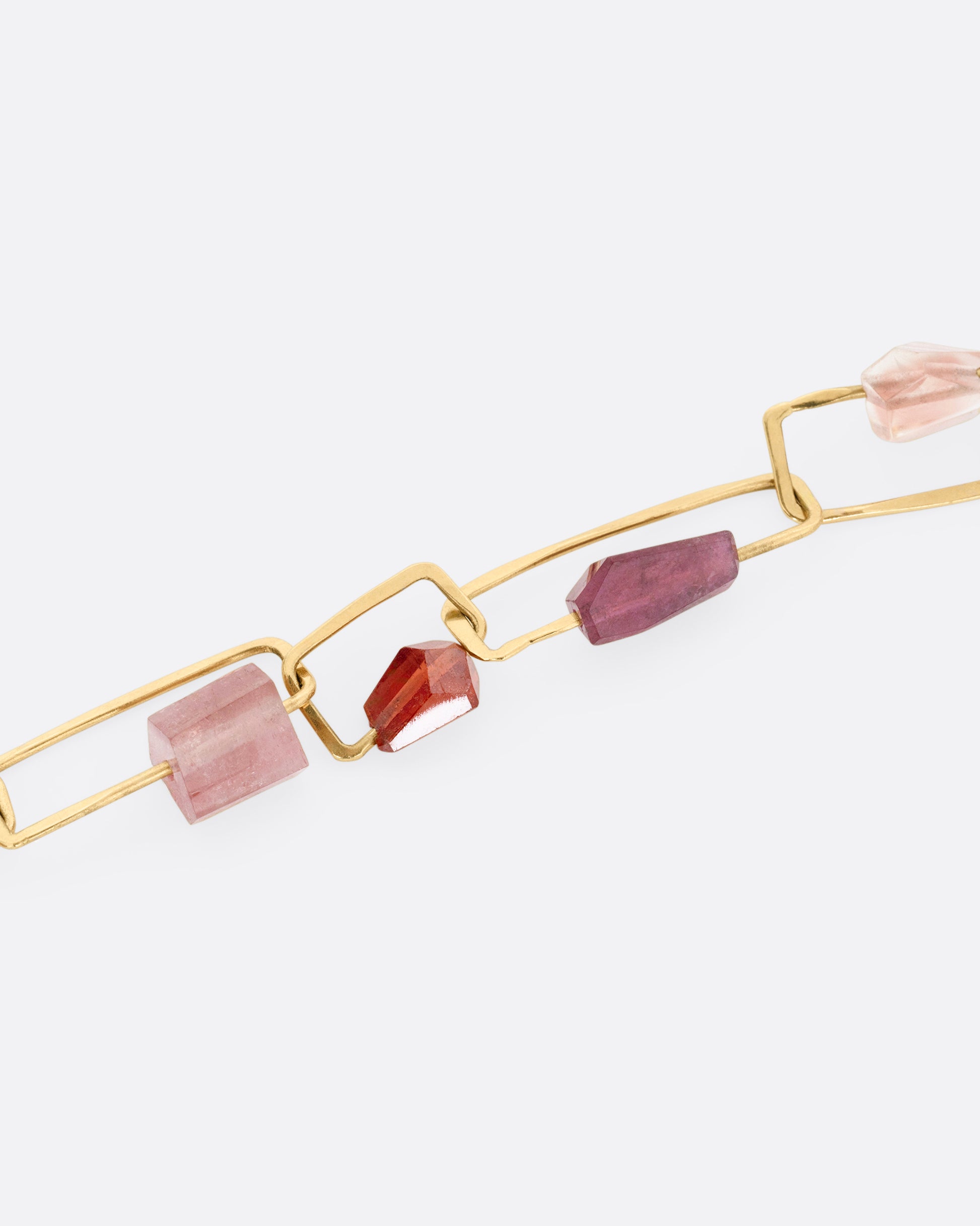 A close up of a yellow gold necklace with hammered paperclip links of differing sizes and freeform tourmalines, hessonite garnets, and Oregon sunstones, shown from the front.