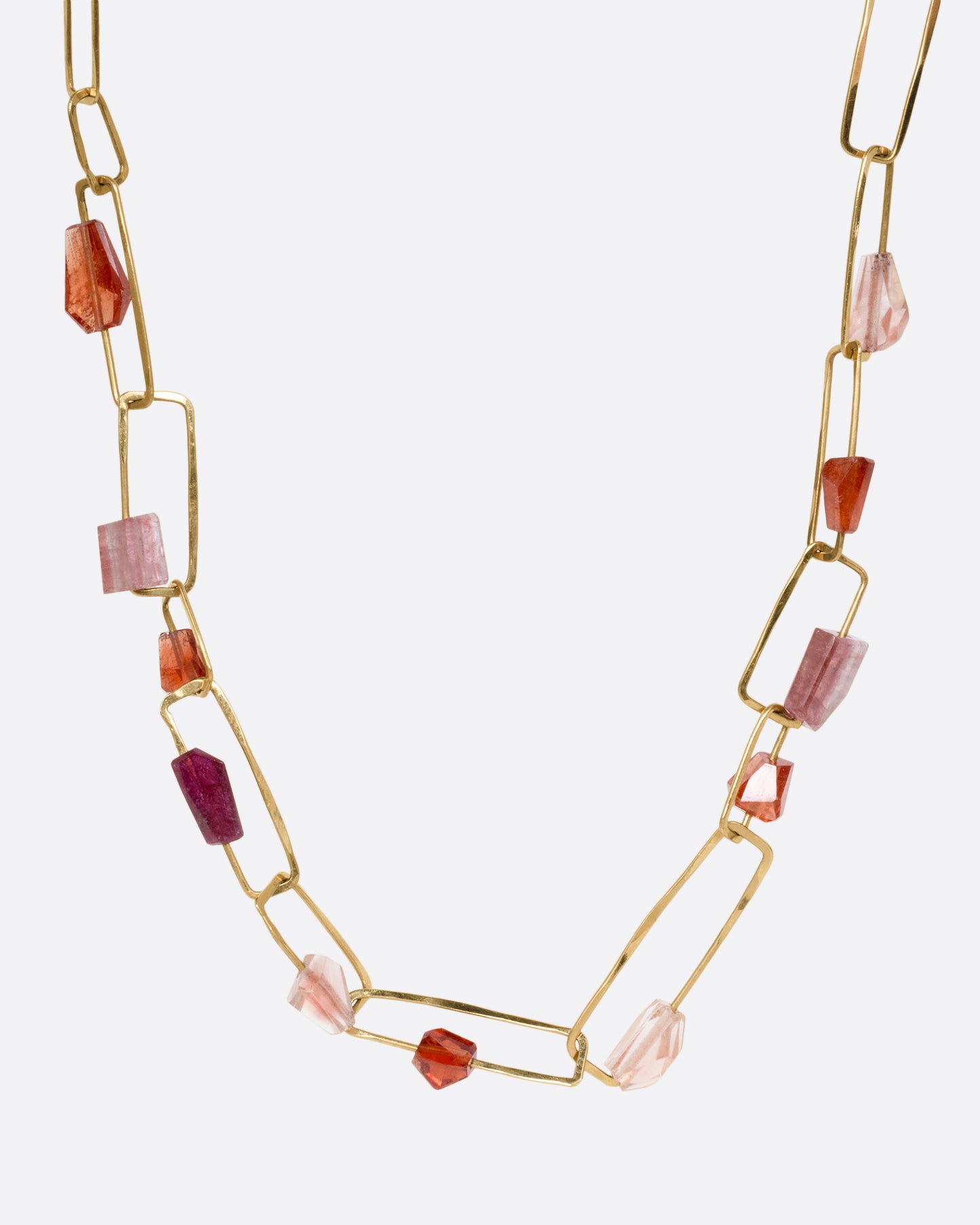 A yellow gold necklace with hammered paperclip links of differing sizes and freeform tourmalines, hessonite garnets, and Oregon sunstones, shown from the front.
