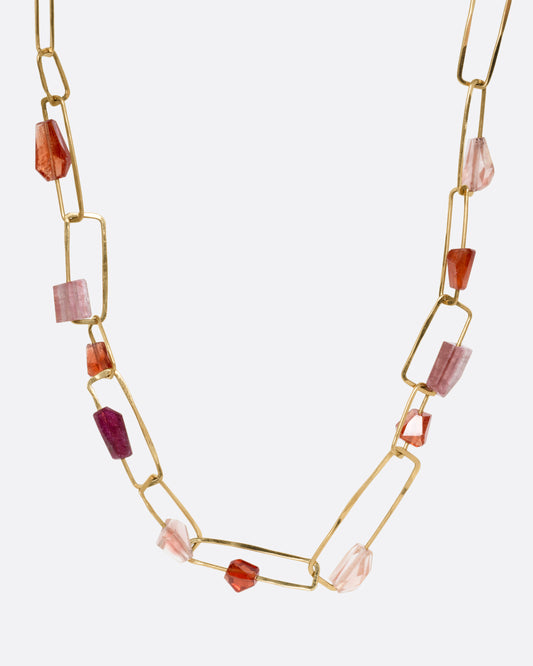A yellow gold necklace with hammered paperclip links of differing sizes and freeform tourmalines, hessonite garnets, and Oregon sunstones, shown from the front.