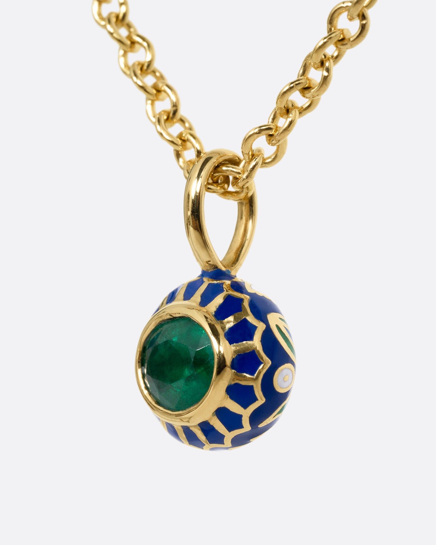 A yellow gold cable chain necklace with a pendant with a blue enamel pattern around an emerald. The pendant has a domed silhouette and floral enamel motif on its reverse. Shown from the side.