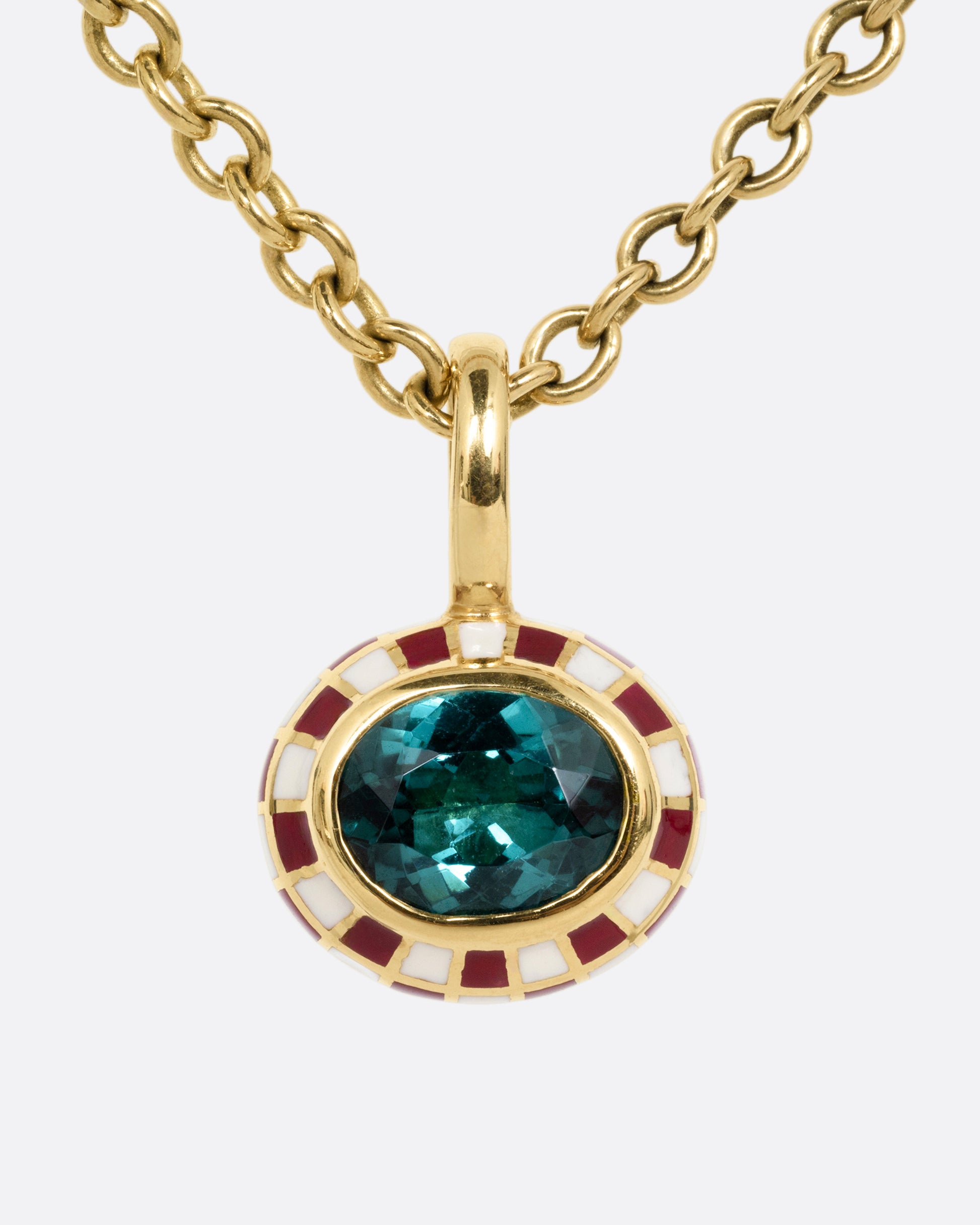 A yellow gold cable chain necklace with a red and cream enamel checkerboard pendant around a green tourmaline. The reverse side of the pendant has a checked pattern. Shown from the front.