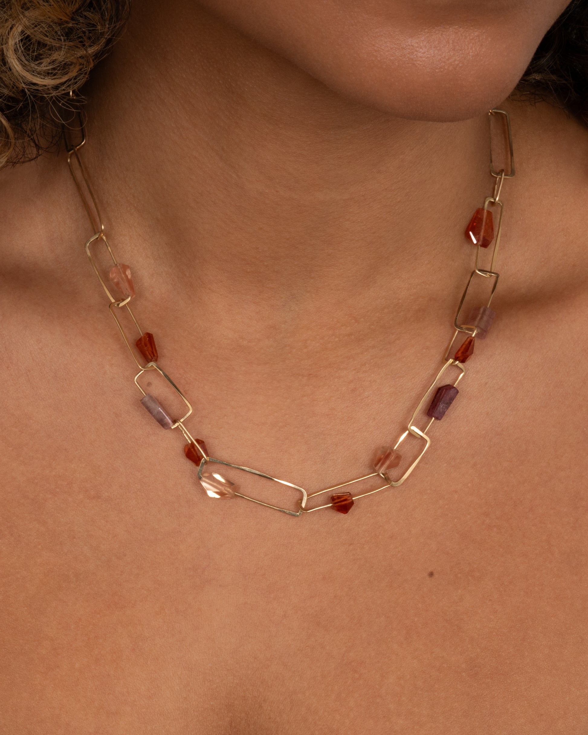 A yellow gold necklace with hammered paperclip links of differing sizes and freeform tourmalines, hessonite garnets, and Oregon sunstones, shown on a person.