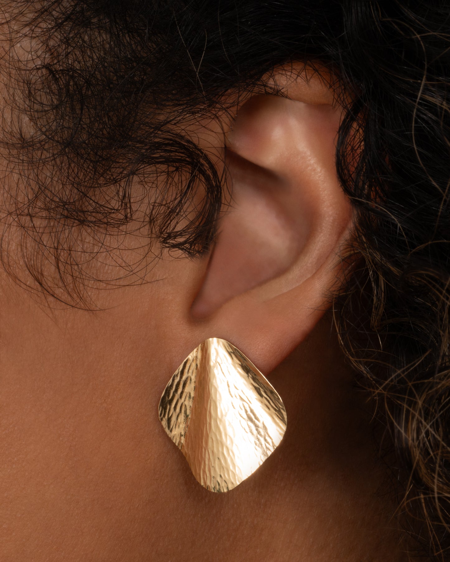 A pair of yellow gold stud earrings with a textural finish and wavy silhouette, shown worn.