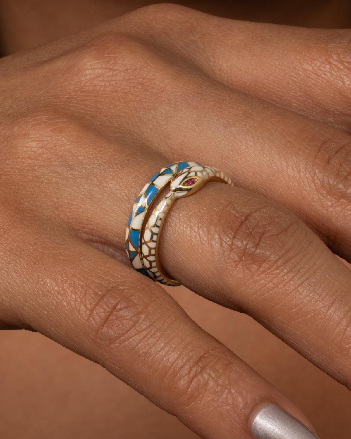 Yellow gold green enamel snake ring, an Ouroboros ring in white and blue enamel shown on a finger for scale