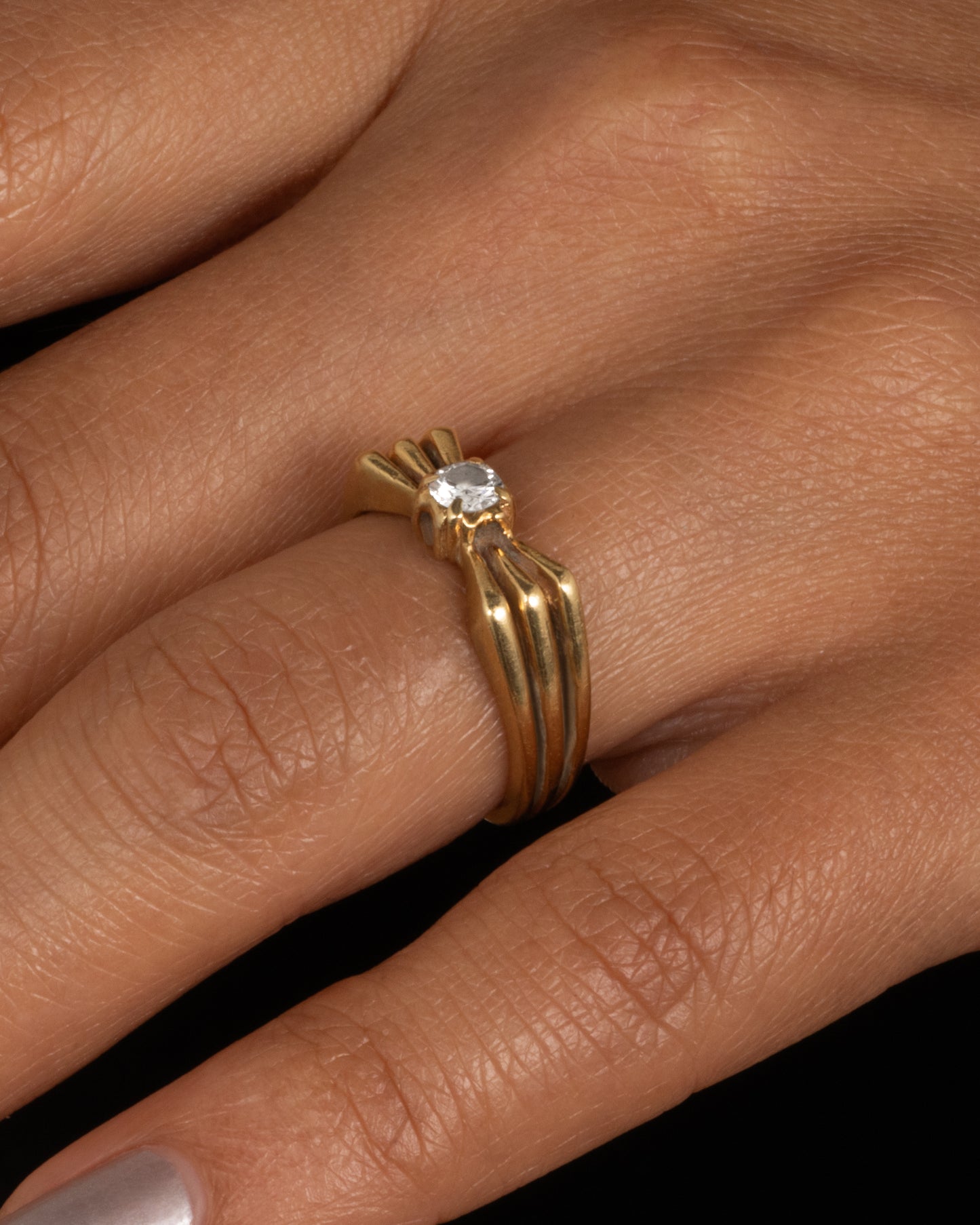 A yellow gold ring with a stacked silhouette and angular shoulders and a prong set diamond at the center. Shown worn.