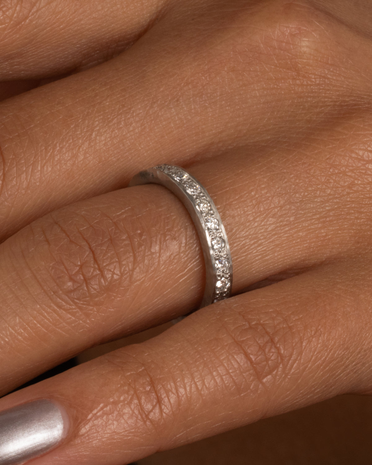 A platinum band with hammered edges and a darkened center with diamonds throughout. Shown worn