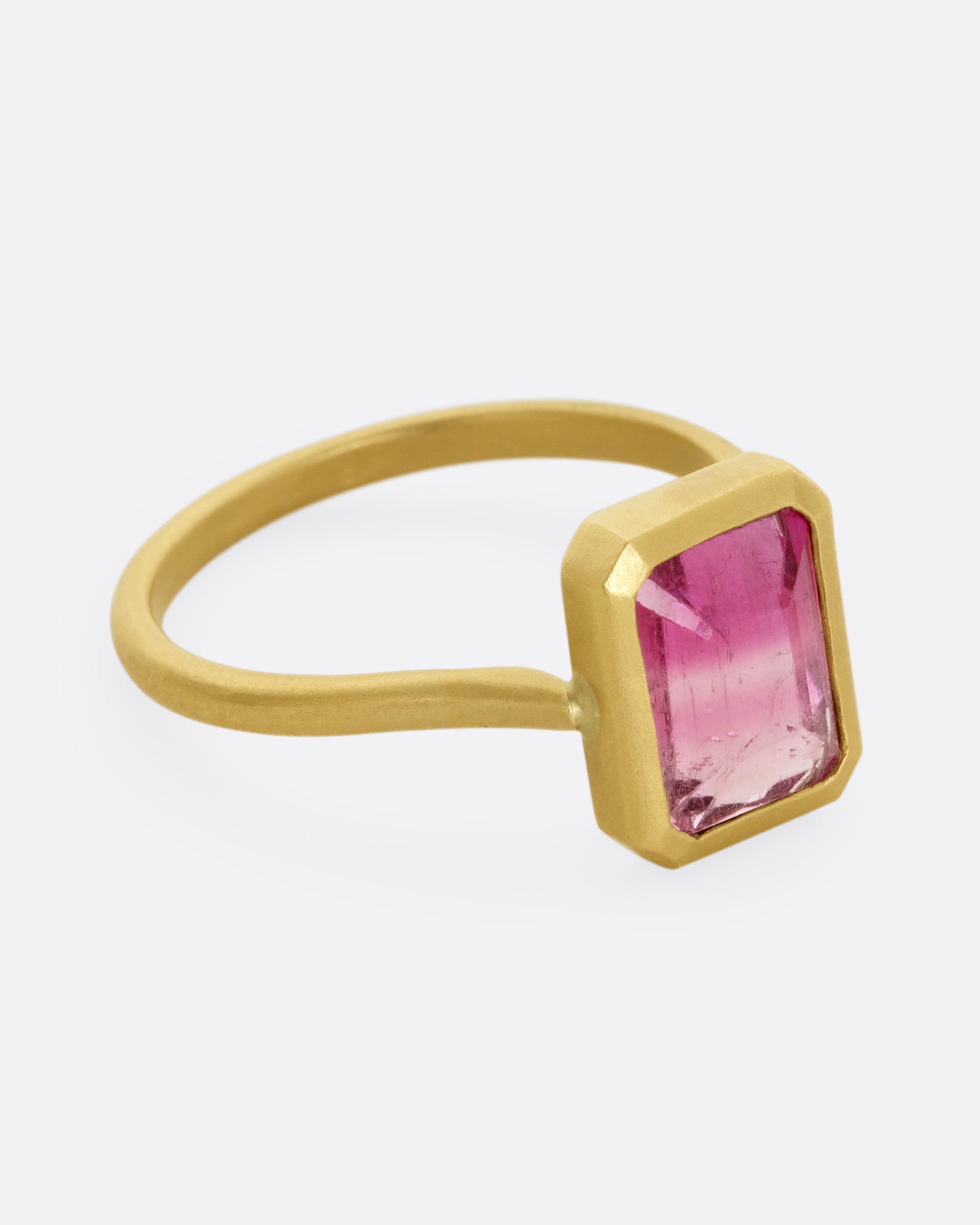 A yellow gold ring with a bezel set rectangular pink bicolor tourmaline. Shown from the side.