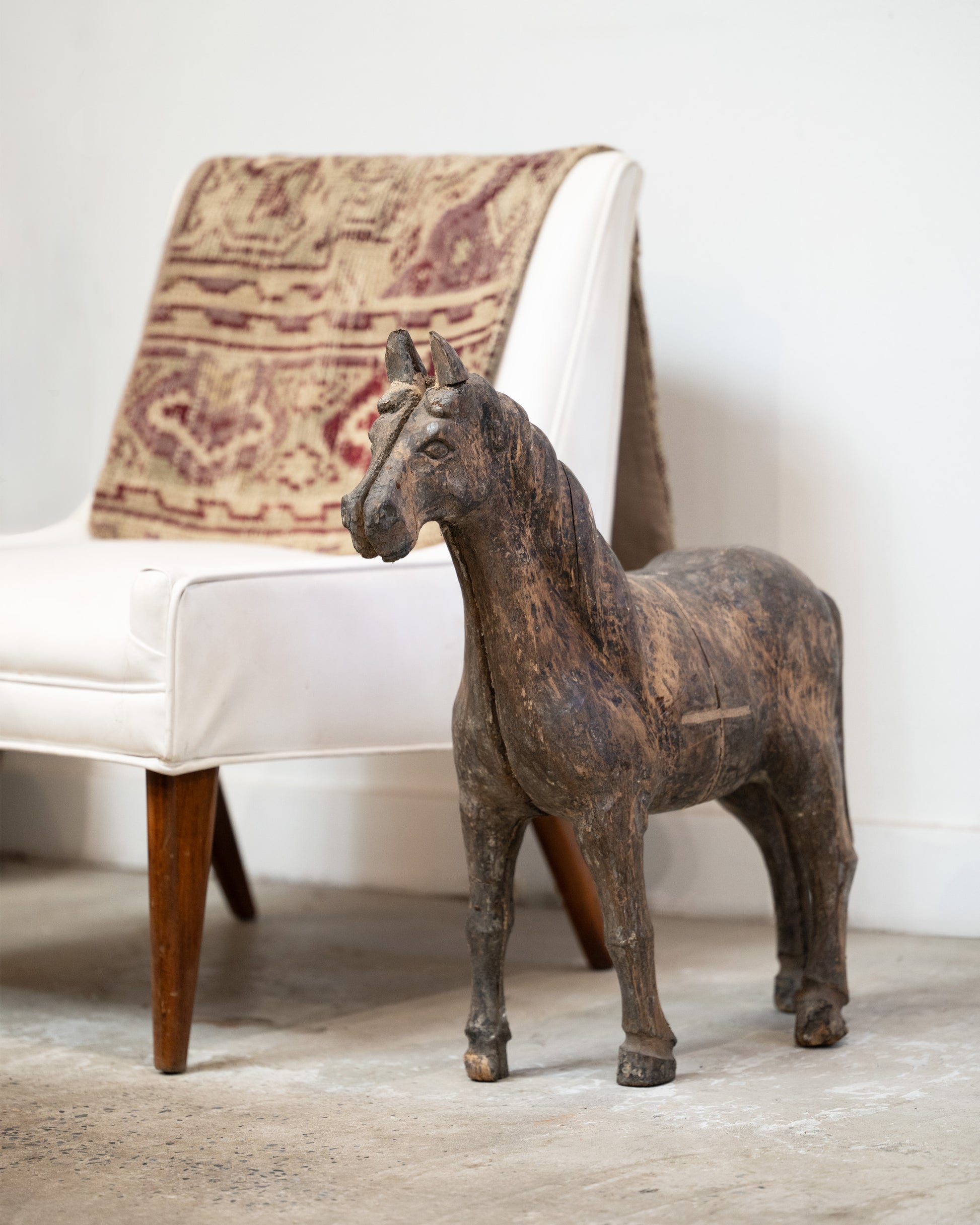 A wooden horse  takaan sculpture shown from the front in front of a white chair.