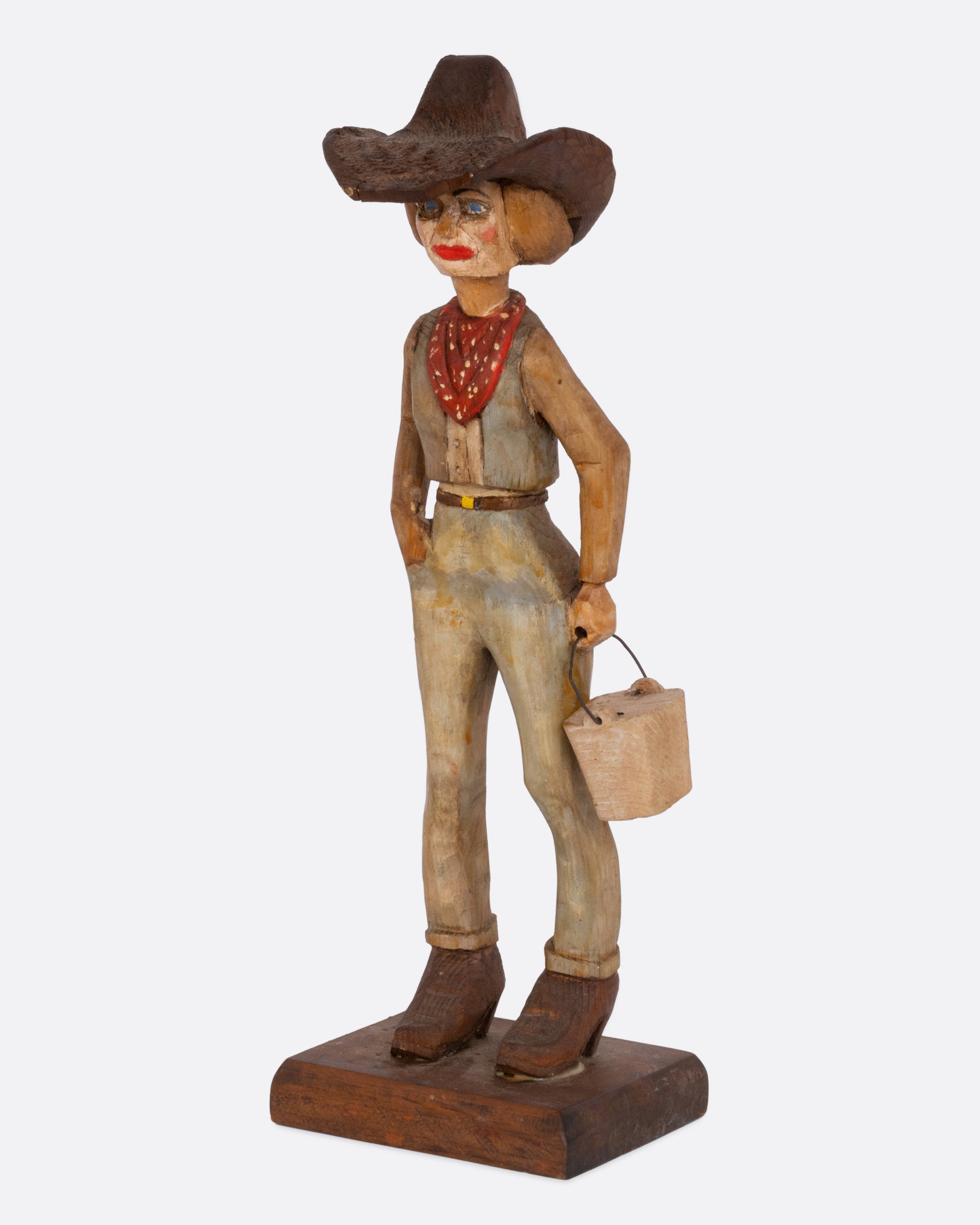  A wooden hand carved and painted folk art cowgirl holding a bucket. Shown from the side.