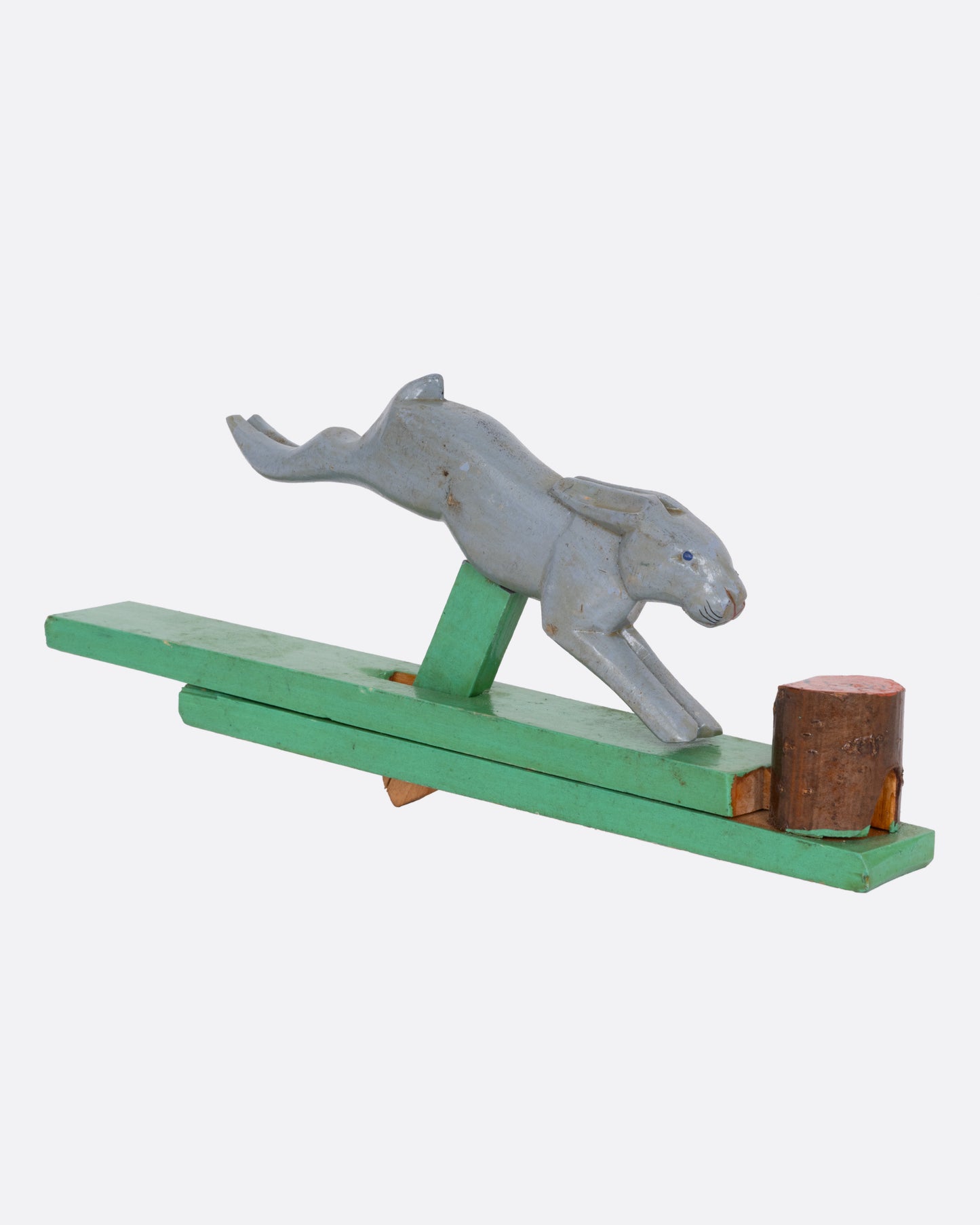 A wooden toy rabbit on a green wooden base, shown from the side.