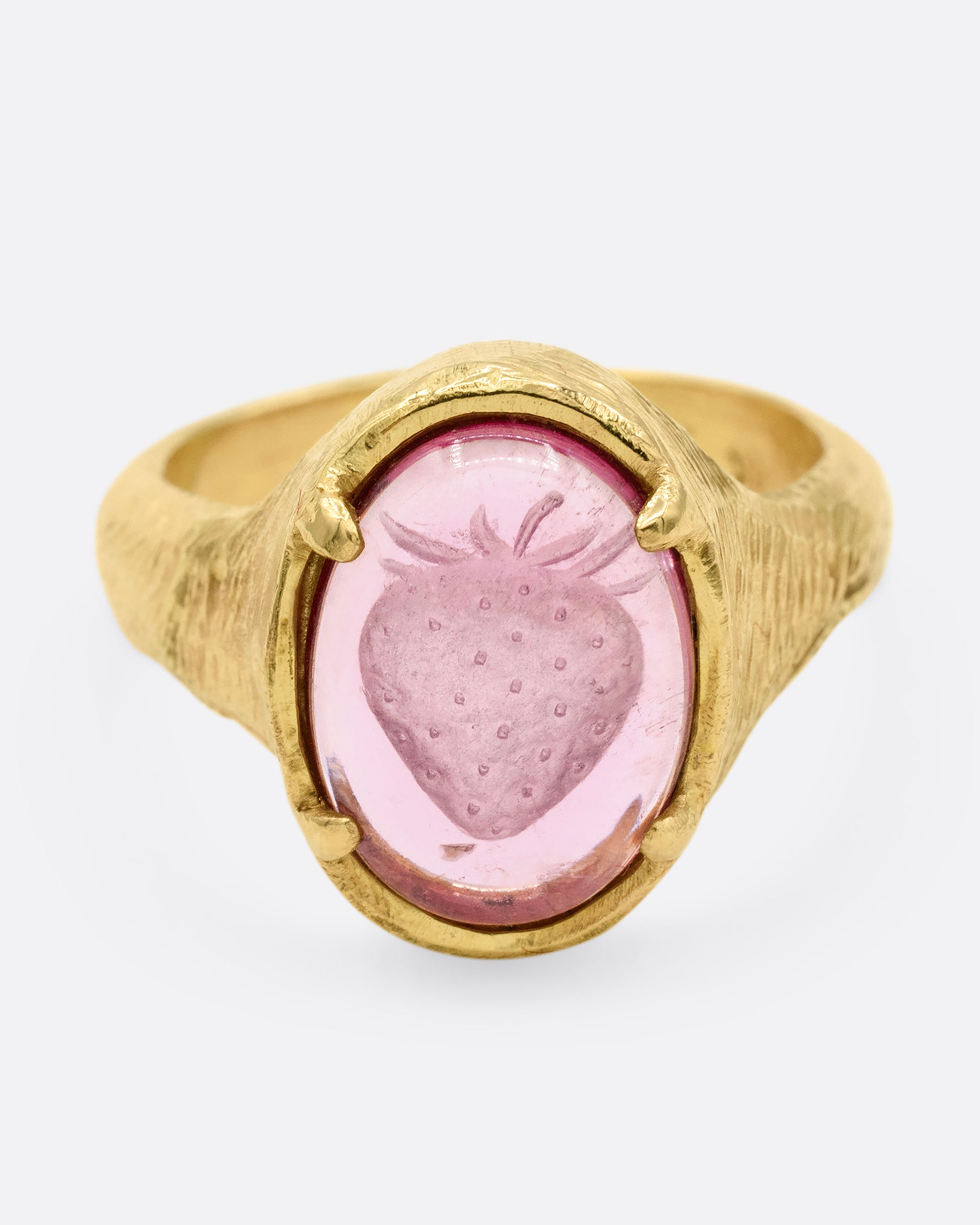 A yellow gold signet ring with a carved strawberry in a prong set pink garnet. Shown from the front.