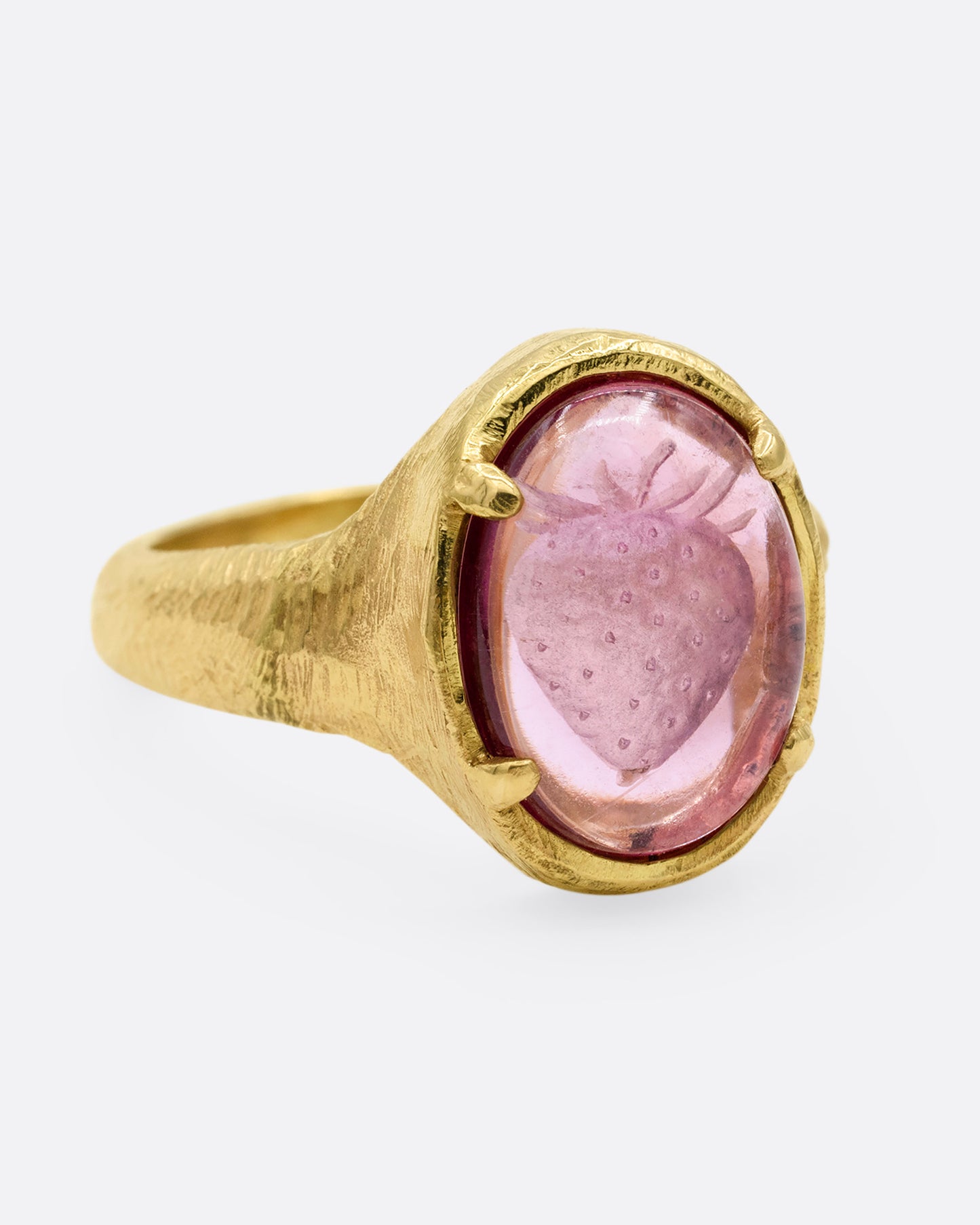 A yellow gold signet ring with a carved strawberry in a prong set pink garnet. Shown from the side.