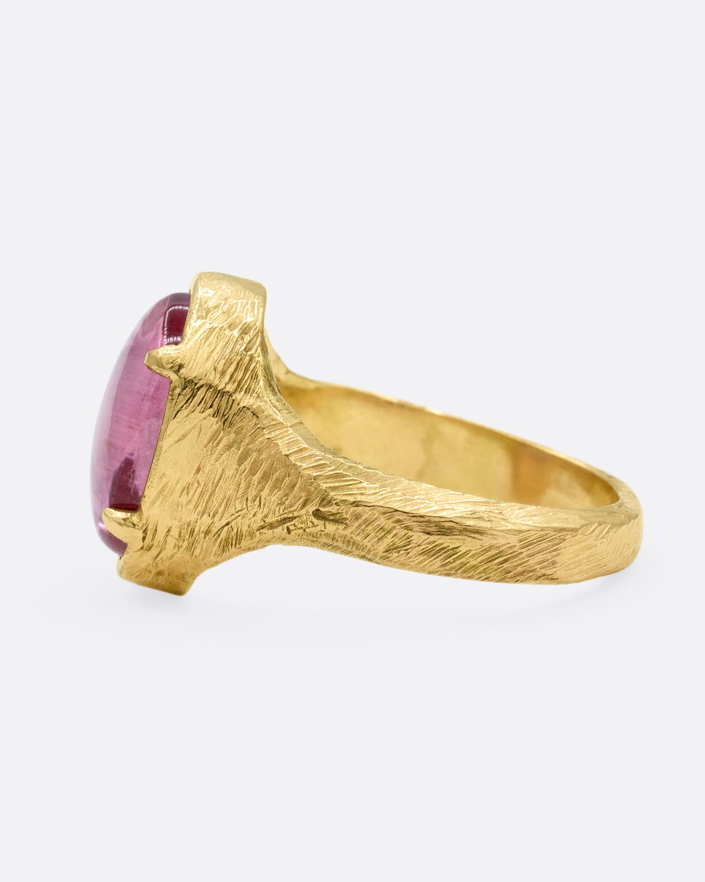 A yellow gold signet ring with a carved strawberry in a prong set pink garnet. Shown from the side.