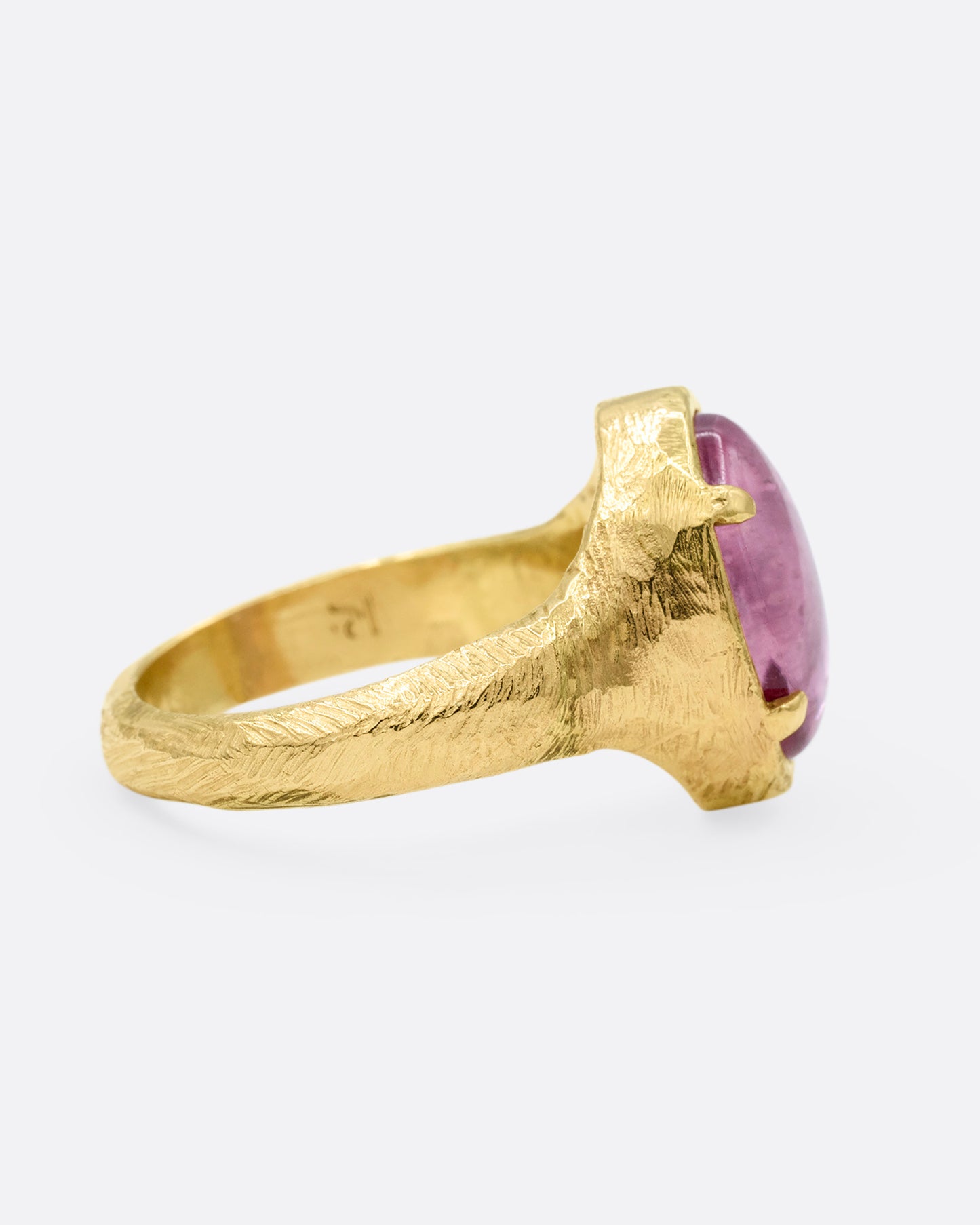 A yellow gold signet ring with a carved strawberry in a prong set pink garnet. Shown from the side.