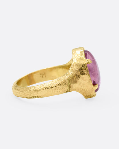 A yellow gold signet ring with a carved strawberry in a prong set pink garnet. Shown from the side.