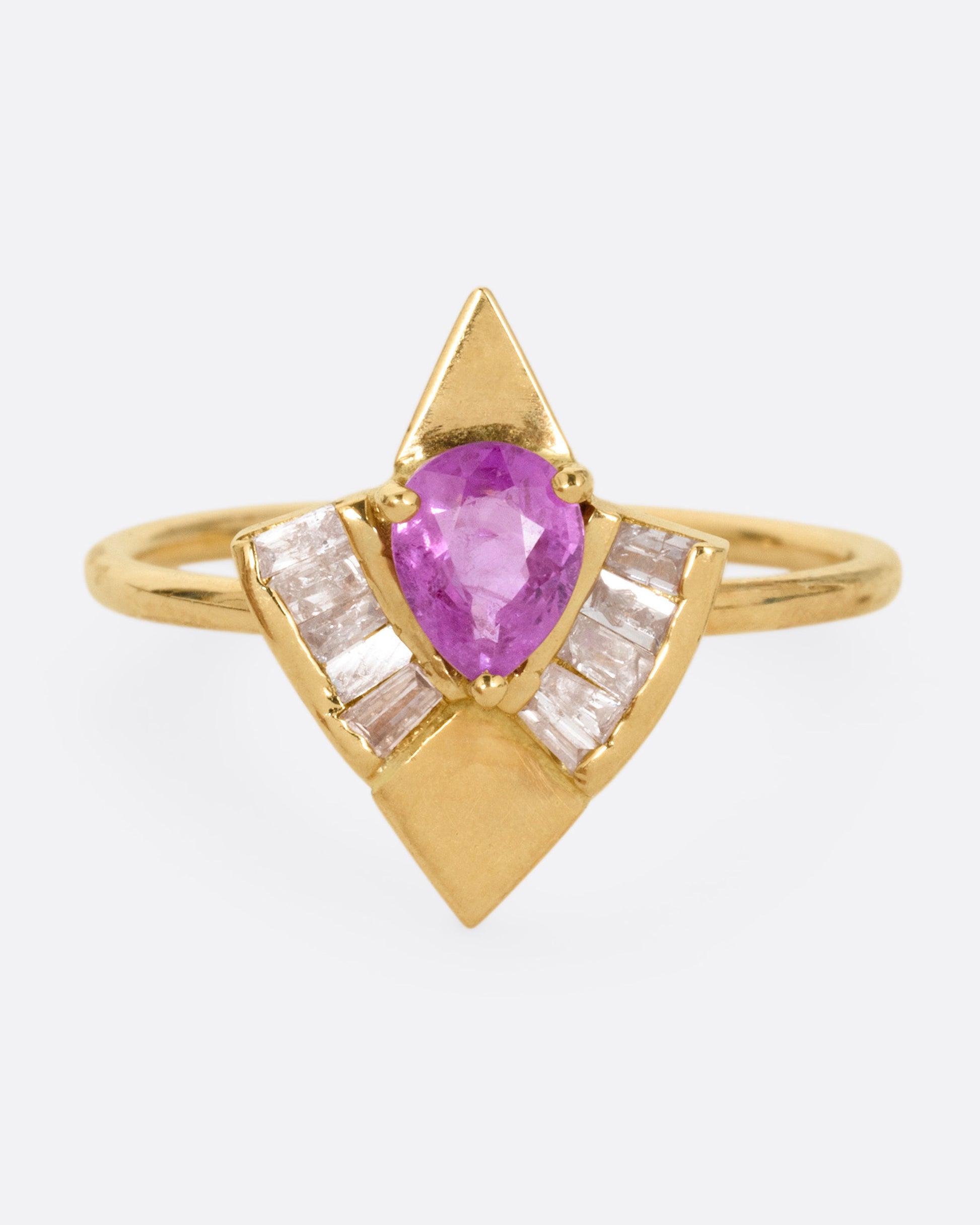 A yellow gold ring with a pink sapphire and baguette diamonds, shown from the front.