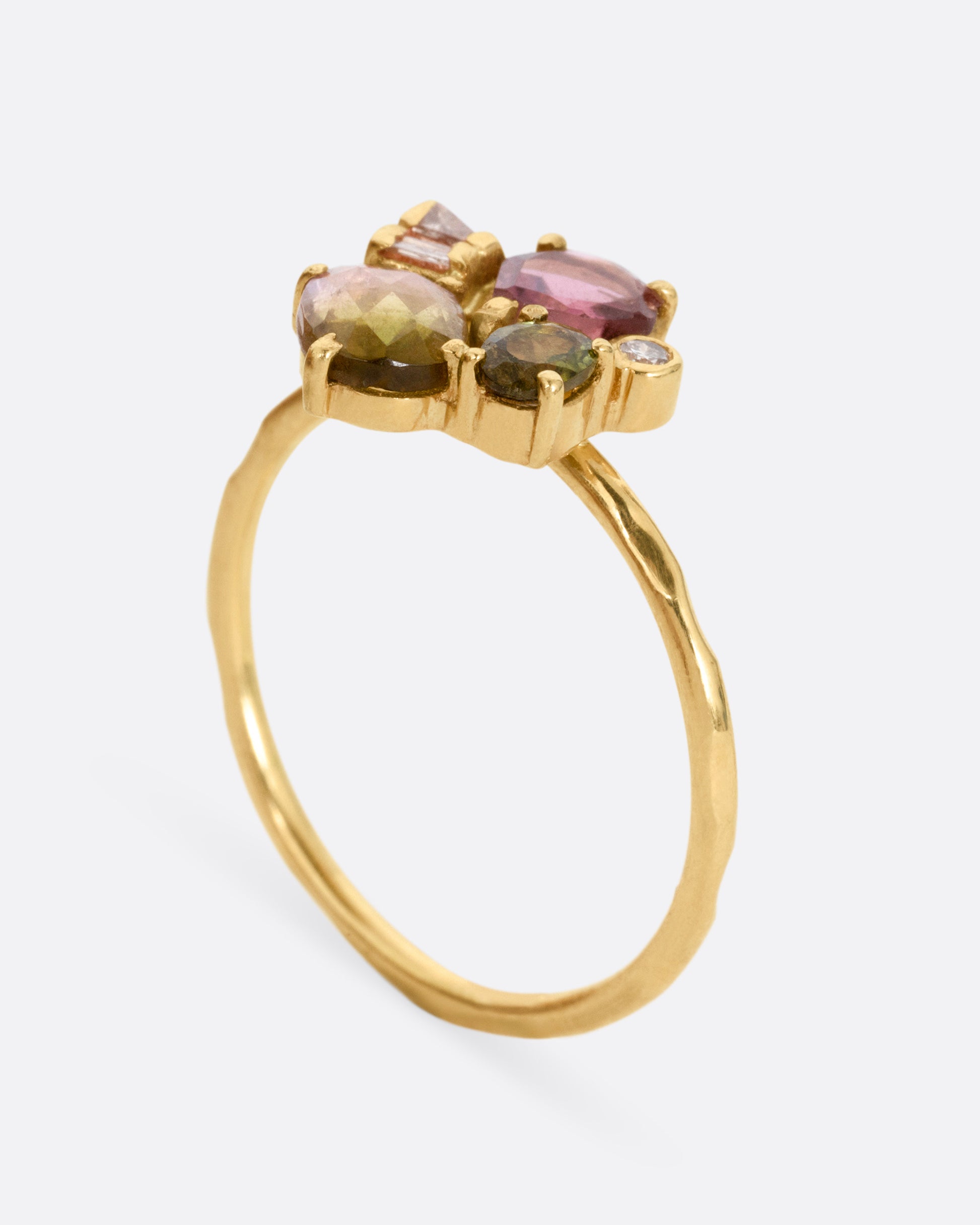 A yellow gold ring with green and pink tourmalines and three diamonds. Shown from the side standing up.